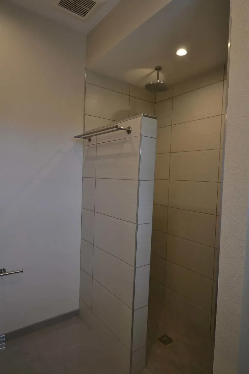 Walk-in shower with tiled walls and a partial divider, a towel rack, and a rain showerhead.