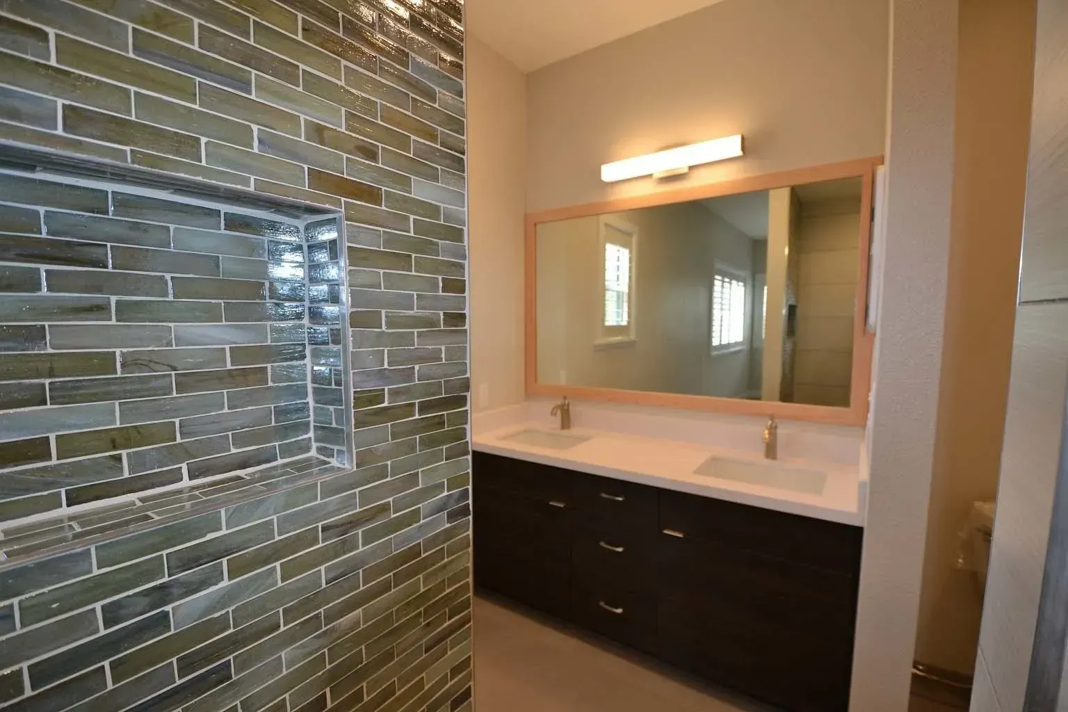 Bathroom with green tiled shower, dark wood vanity with double sinks, and a large mirror.