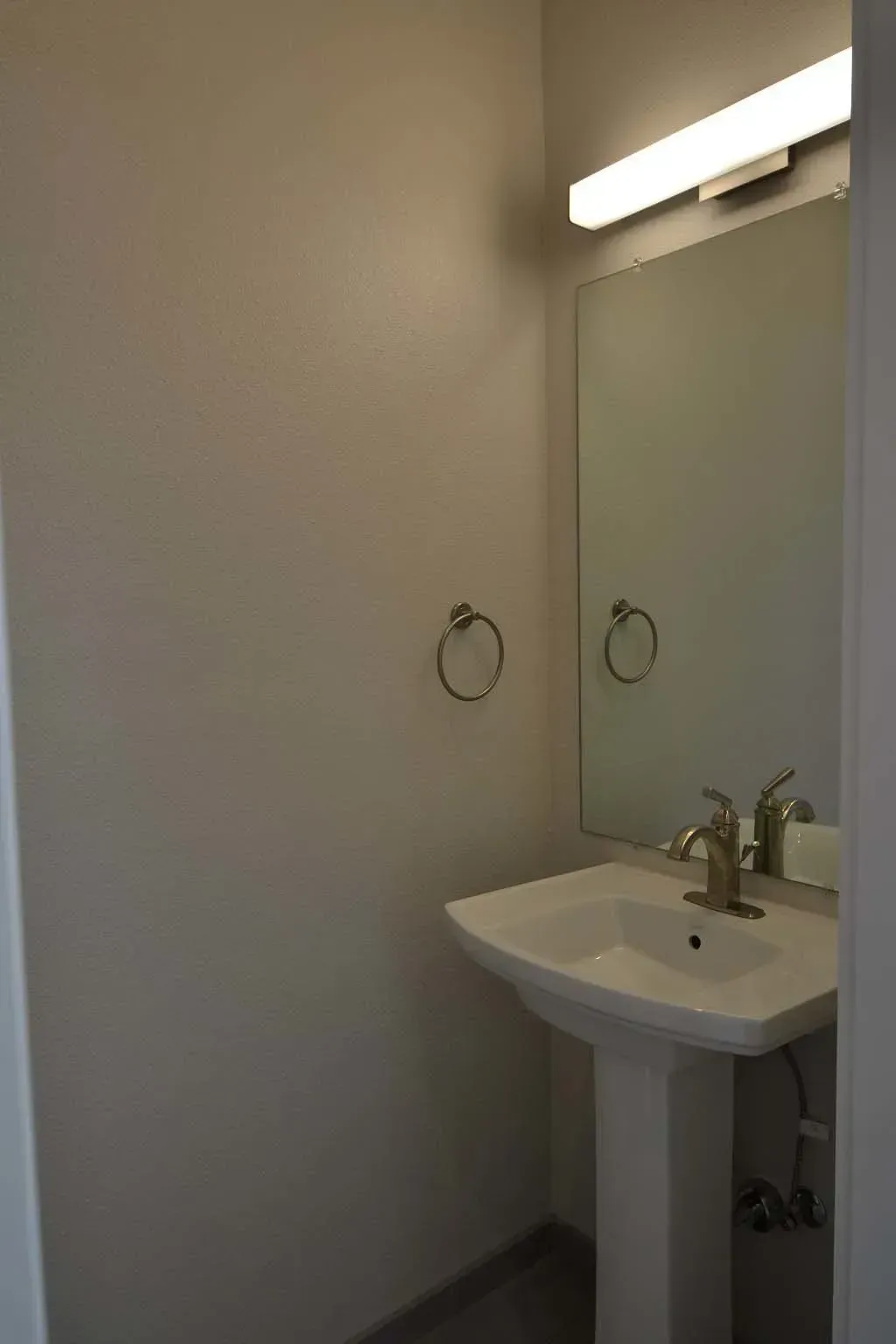 Bathroom with pedestal sink, mirror, towel ring, and overhead light.
