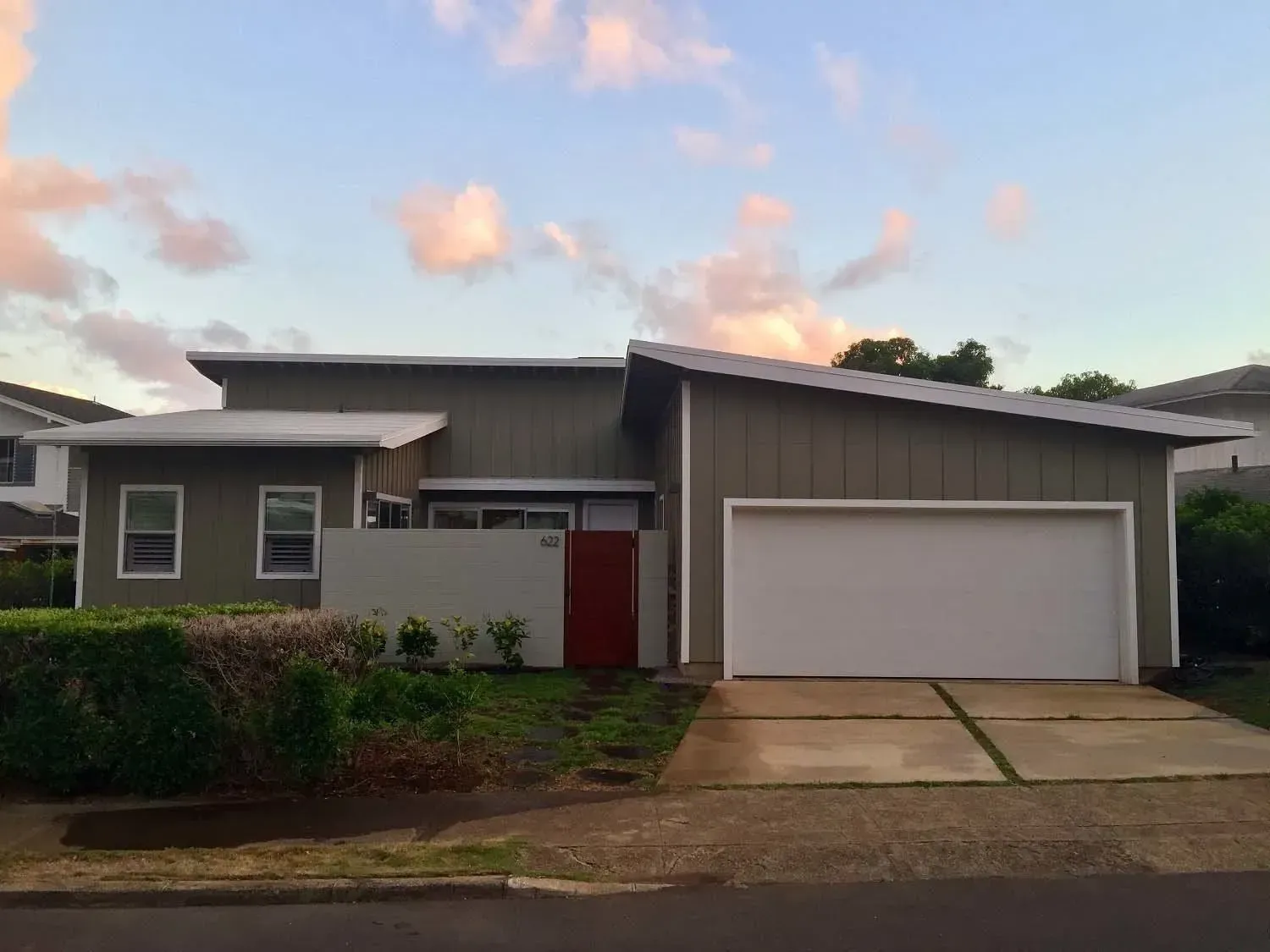 Modern, green house with white garage door and red front door, set against a cloudy sky.