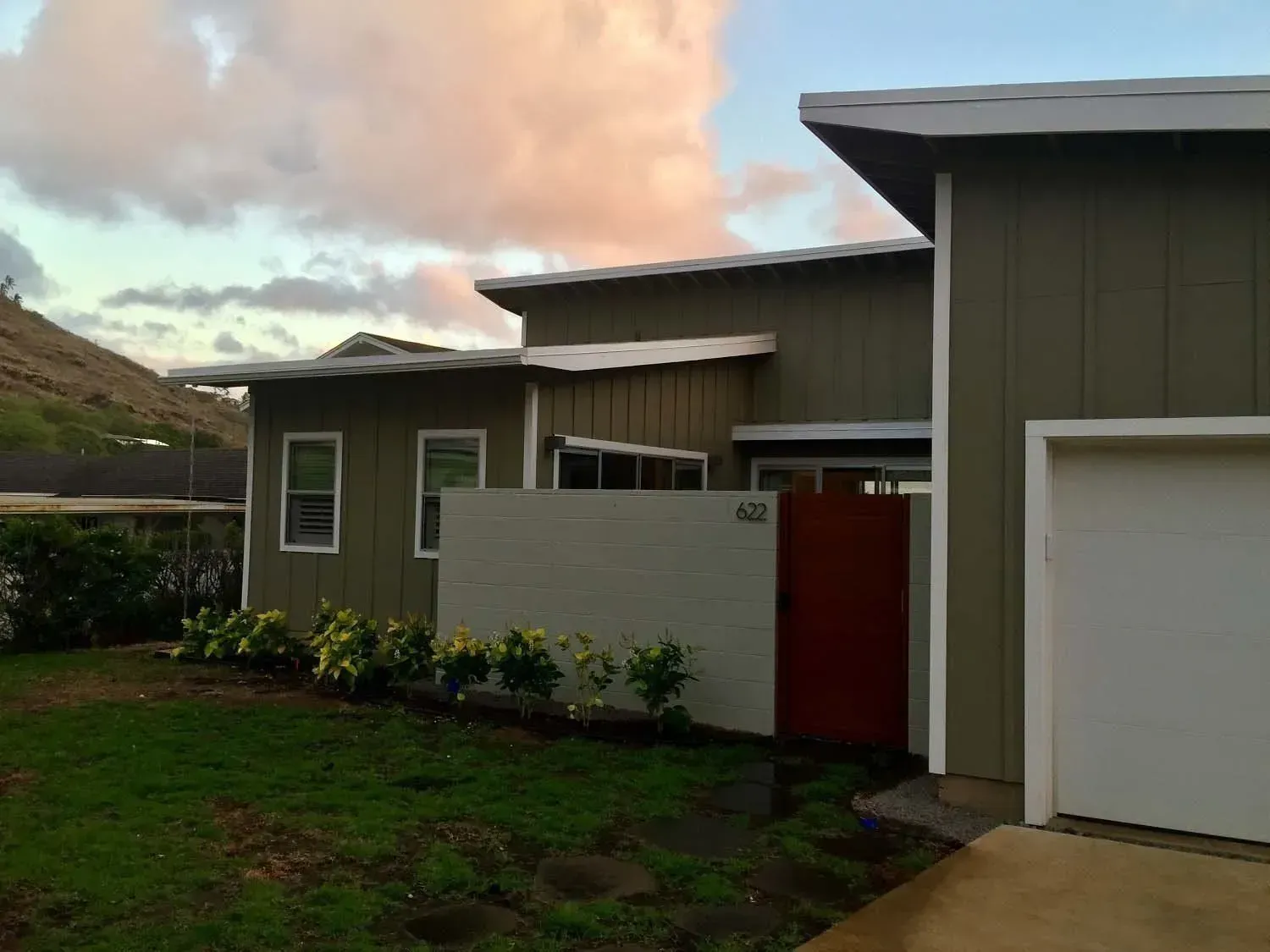 Green house with white garage door, concrete wall, and red gate; cloudy sky.