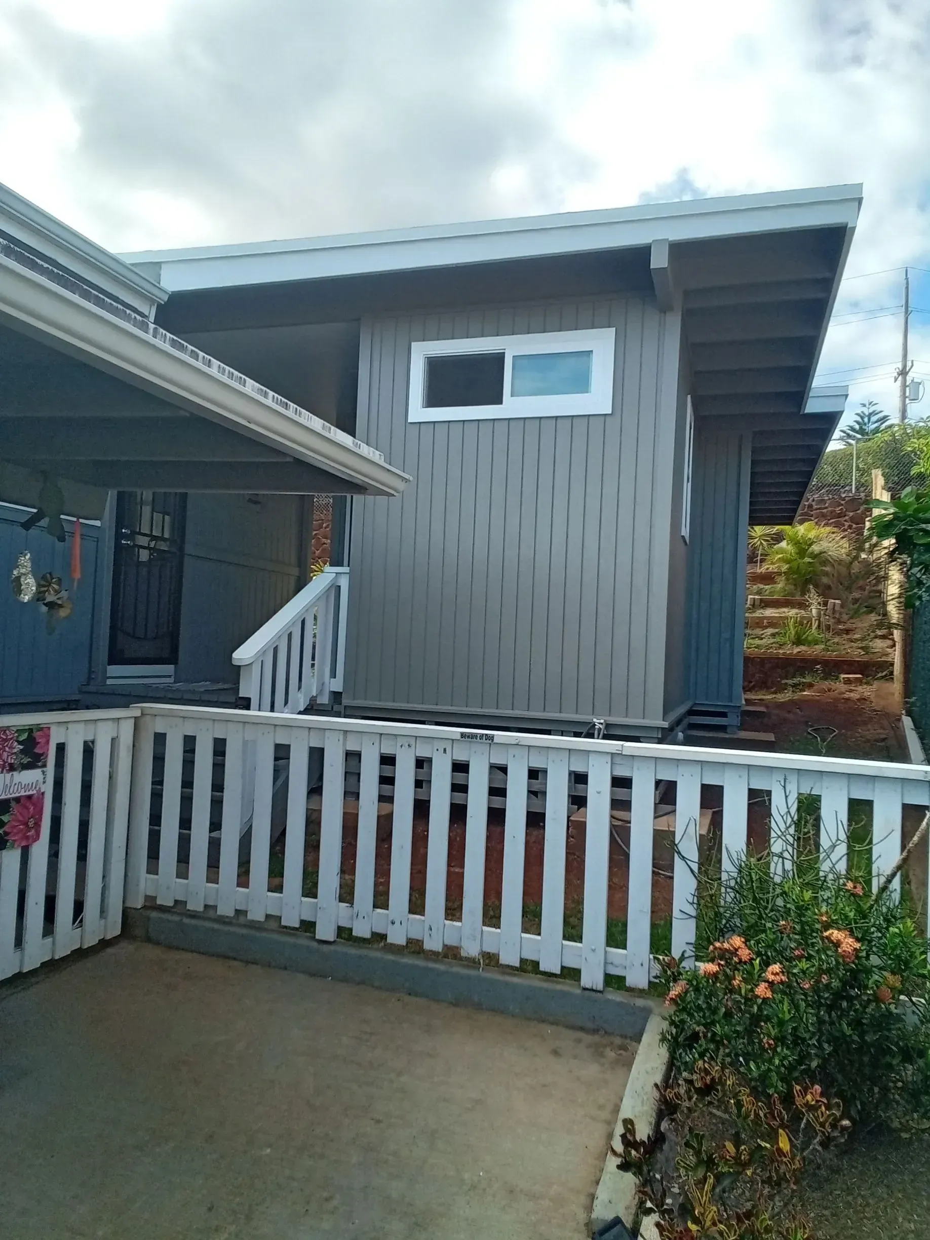 Gray house with white trim, a small window, and a white picket fence on a cloudy day.