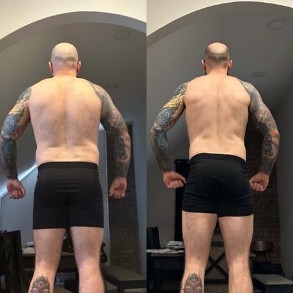 A shirtless man with tattoos on his arms and legs is standing in a living room