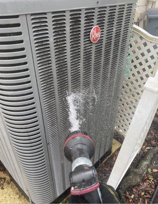 A person is spraying water on an air conditioner with a hose.
