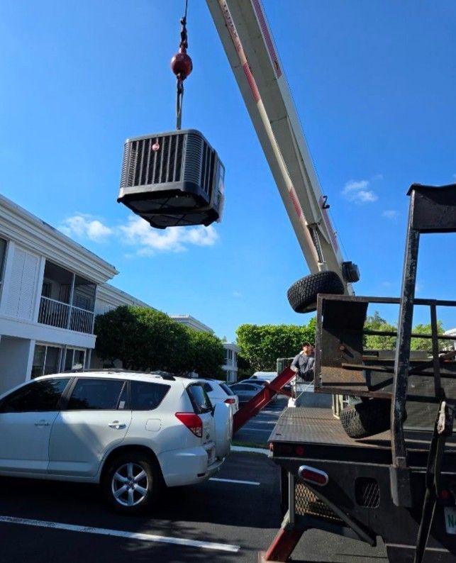 An air conditioner is being lifted by a crane in a parking lot