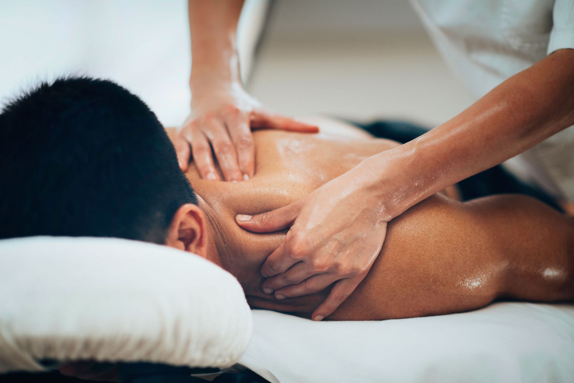 Person receiving a back massage; therapist's hands kneading oiled skin on the shoulder and back.