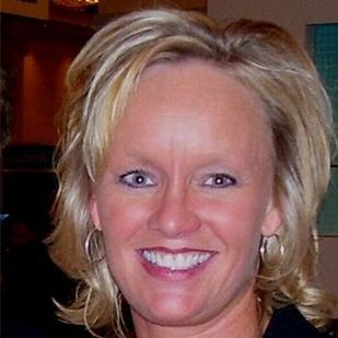 Susan Wurtele smiling, wearing hoop earrings, in a dimly lit setting.