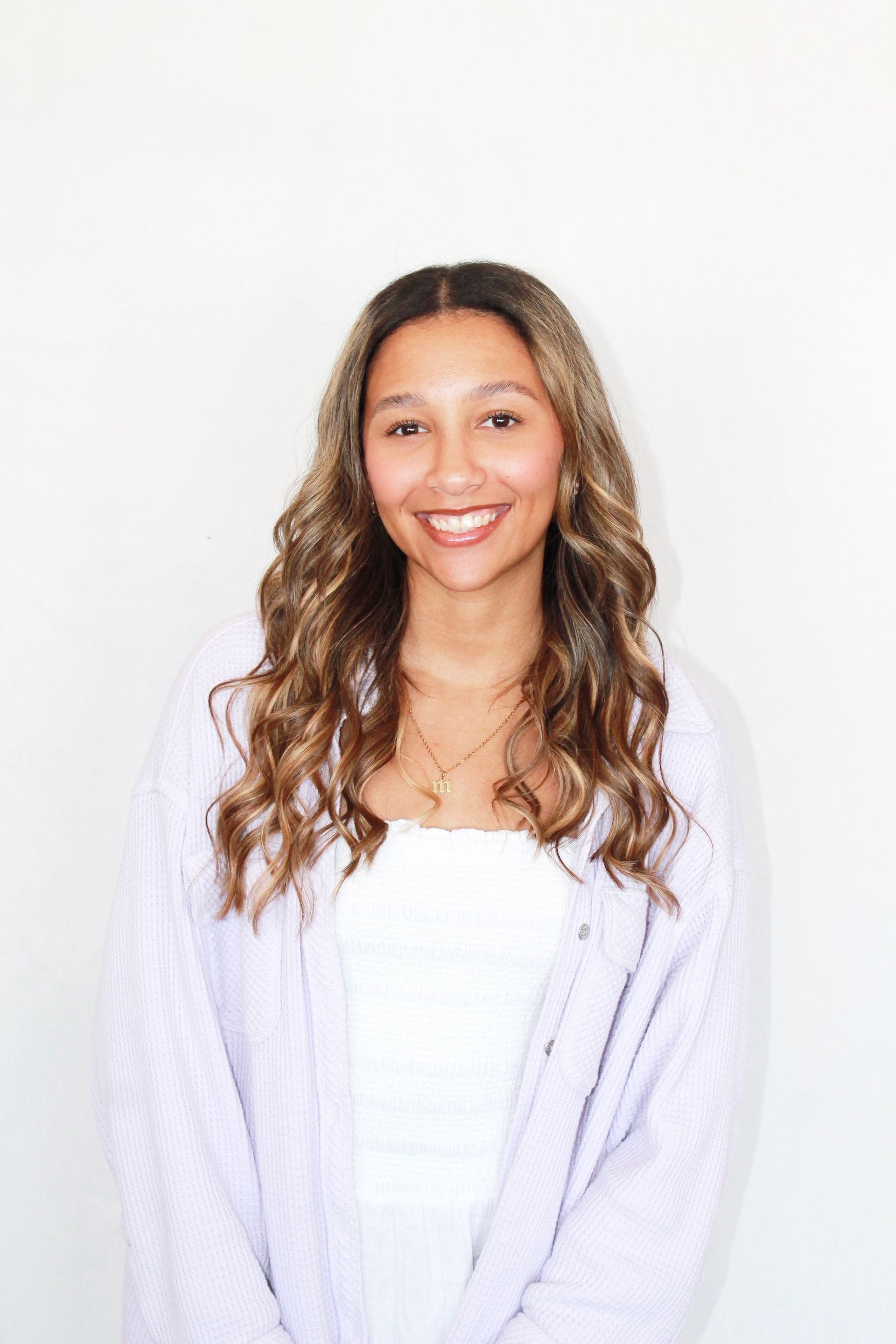 Nikki Bates smiling, writing on a clipboard, wearing glasses and a beige sweater, against a white background.