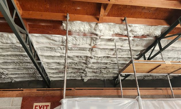 Ceiling under construction with exposed beams, insulation, and hanging scaffolding poles