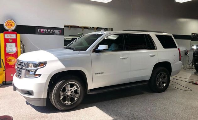 A white Chevrolet Tahoe SUV parked inside a workshop, next to a vintage-style red and yellow gas pump.