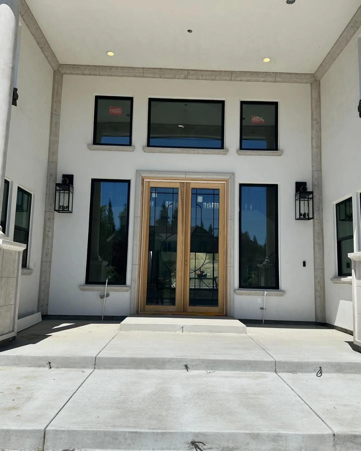 Modern home entrance featuring a wood double door, symmetrical windows, white stucco walls, and concrete steps.