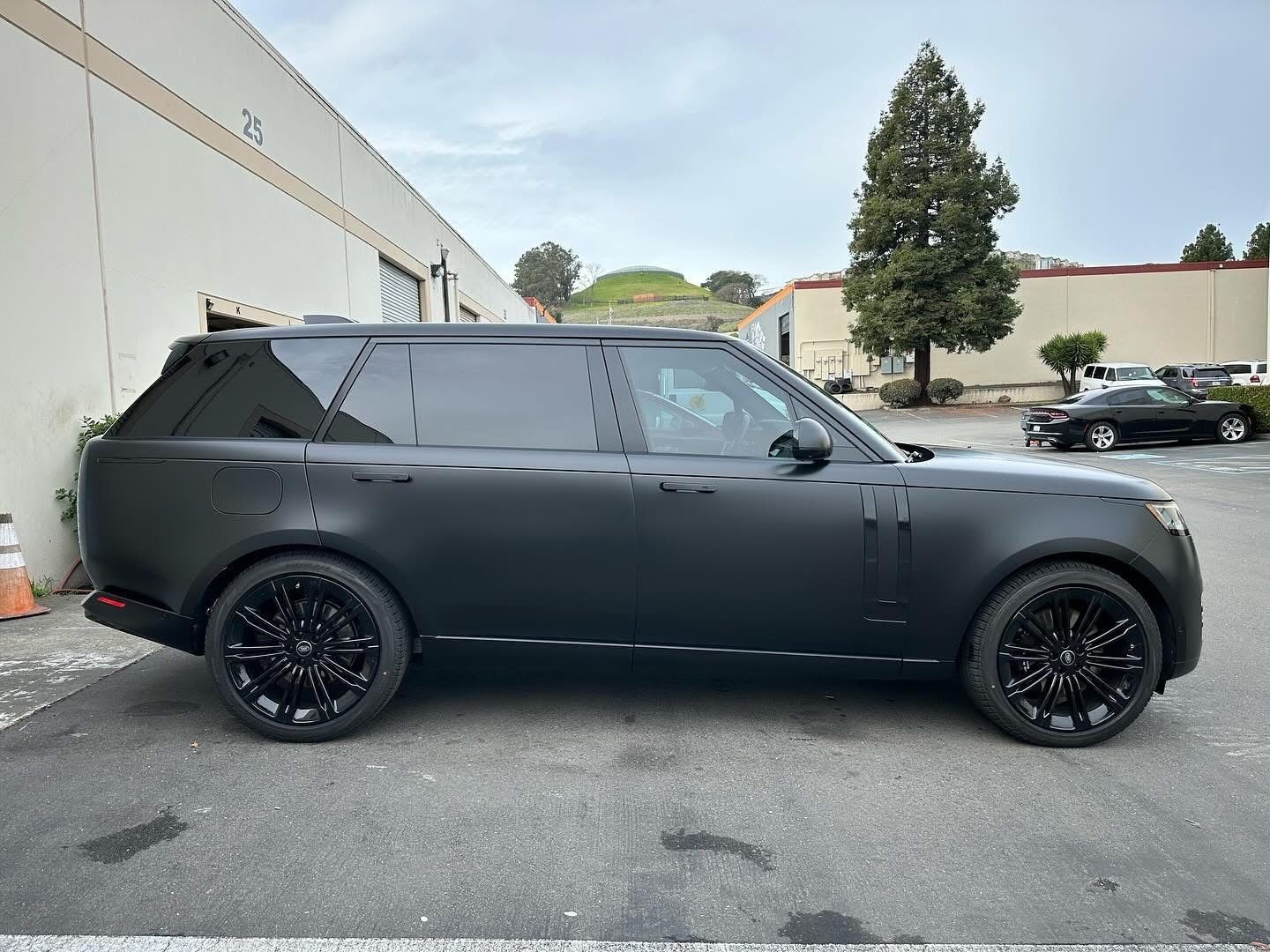 A matte black Range Rover parked on a paved lot beside an industrial building.