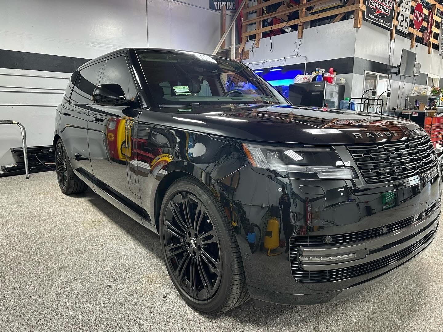 A sleek, glossy black Range Rover SUV parked inside a garage with a workshop background.