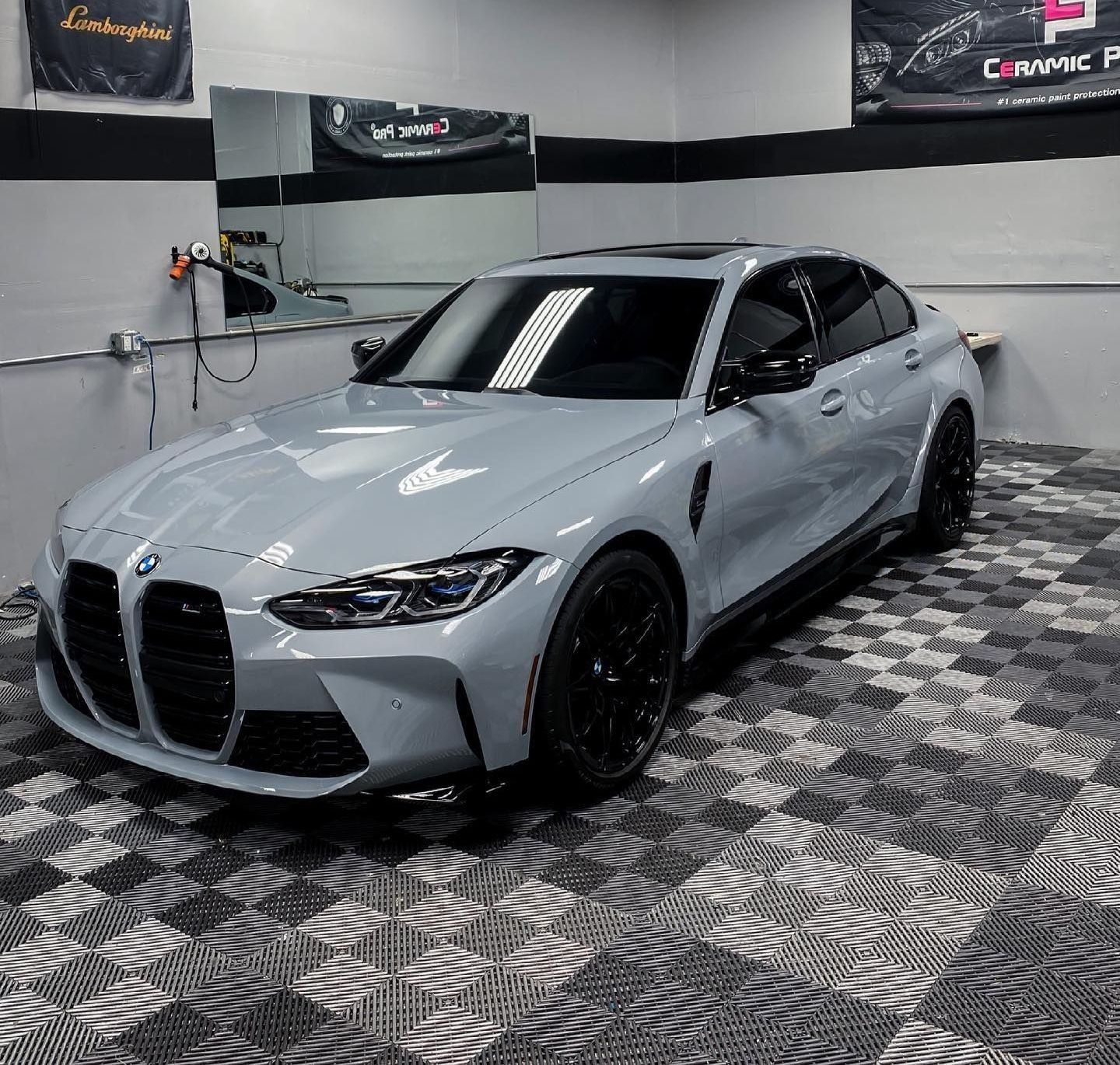 A grey BMW M3 sedan parked on a patterned tile floor inside a professional detailing garage.