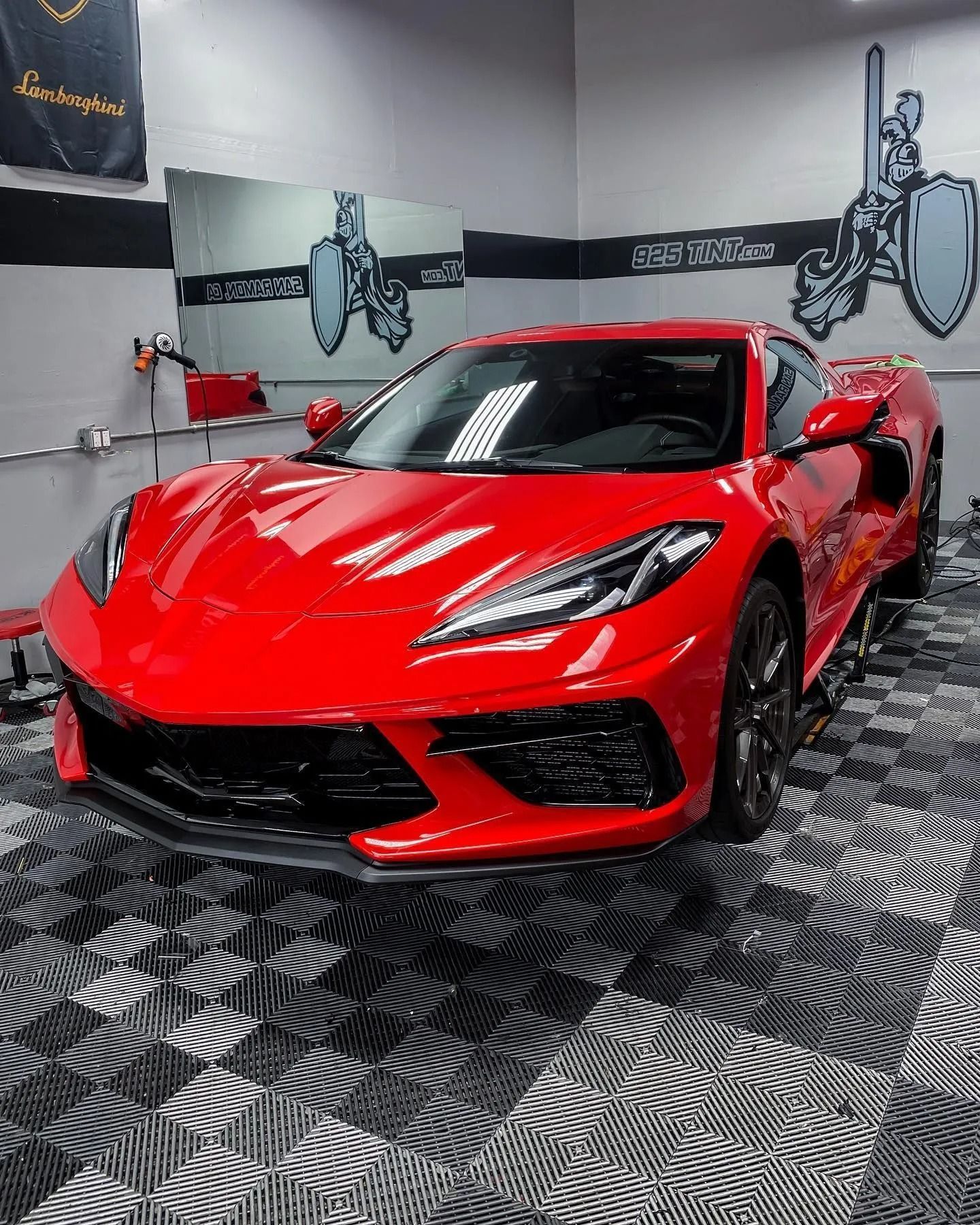 A bright red Chevrolet Corvette sports car parked in a garage with a black and white checkerboard floor.