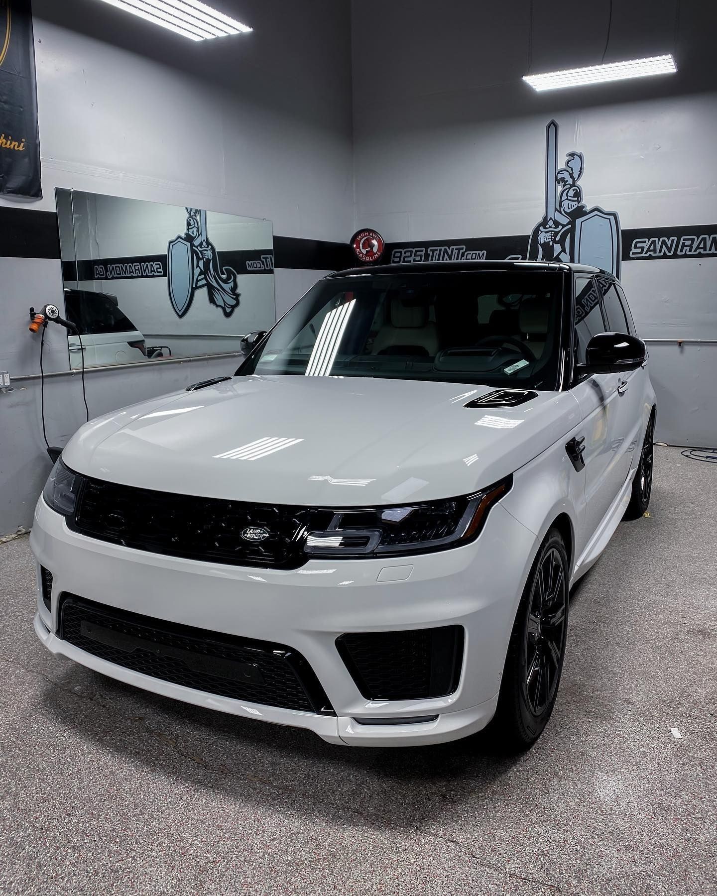 A white Range Rover Sport with black trim parked inside a brightly lit, professional automotive detailing shop.