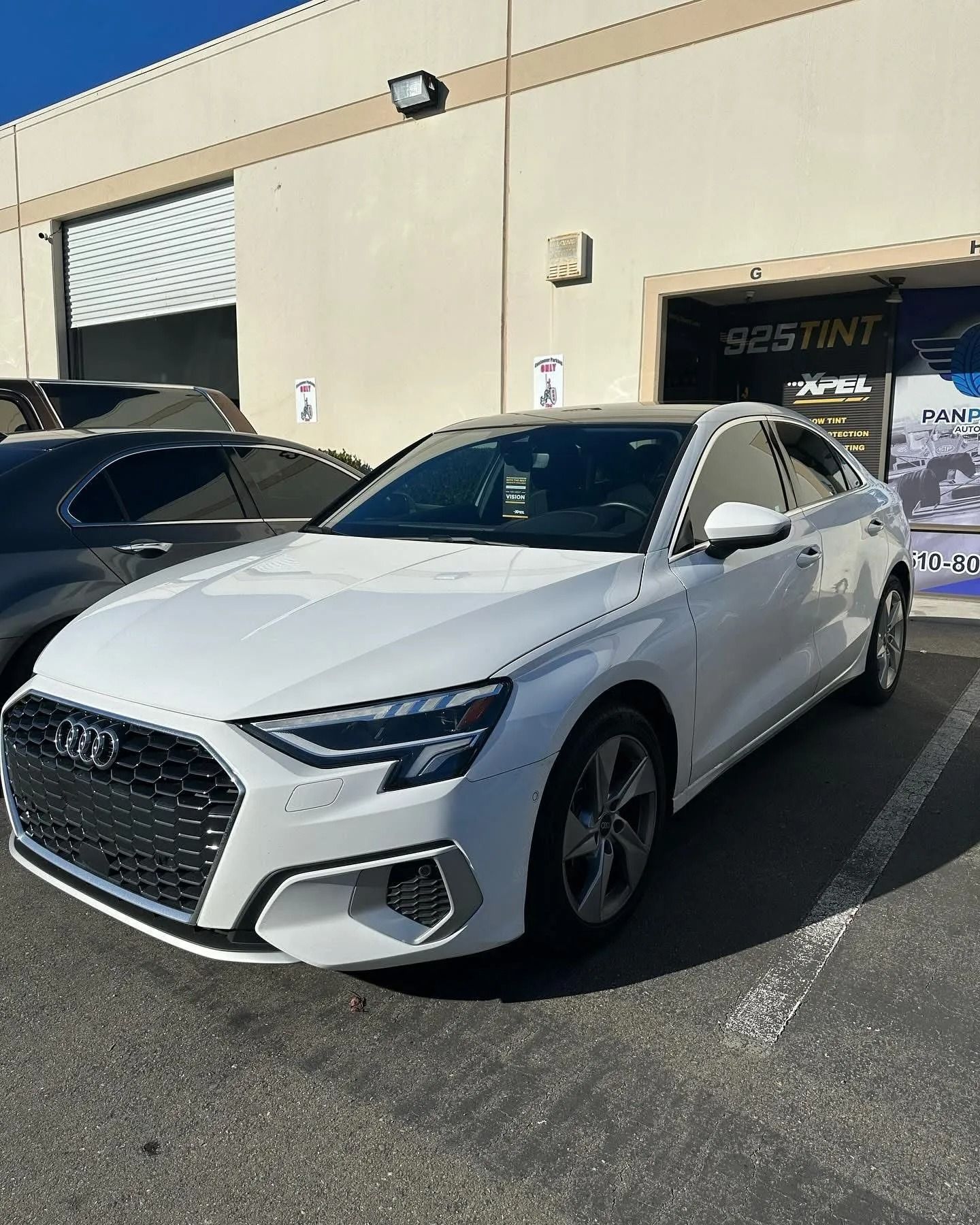 A white Audi sedan parked in front of a building with a tinted window business sign.