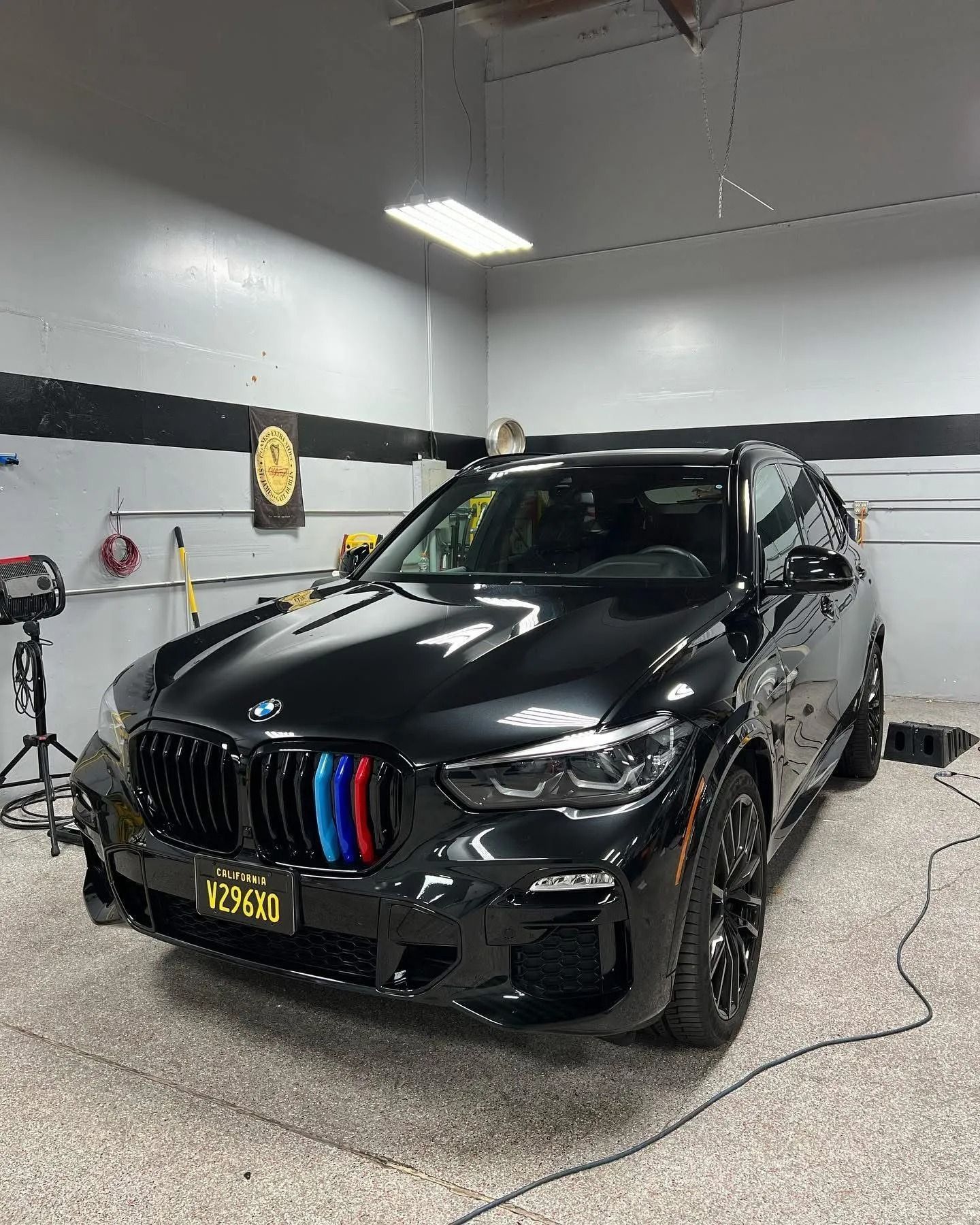 A black BMW SUV parked inside a garage, featuring a front grille with blue, purple, and red stripes.