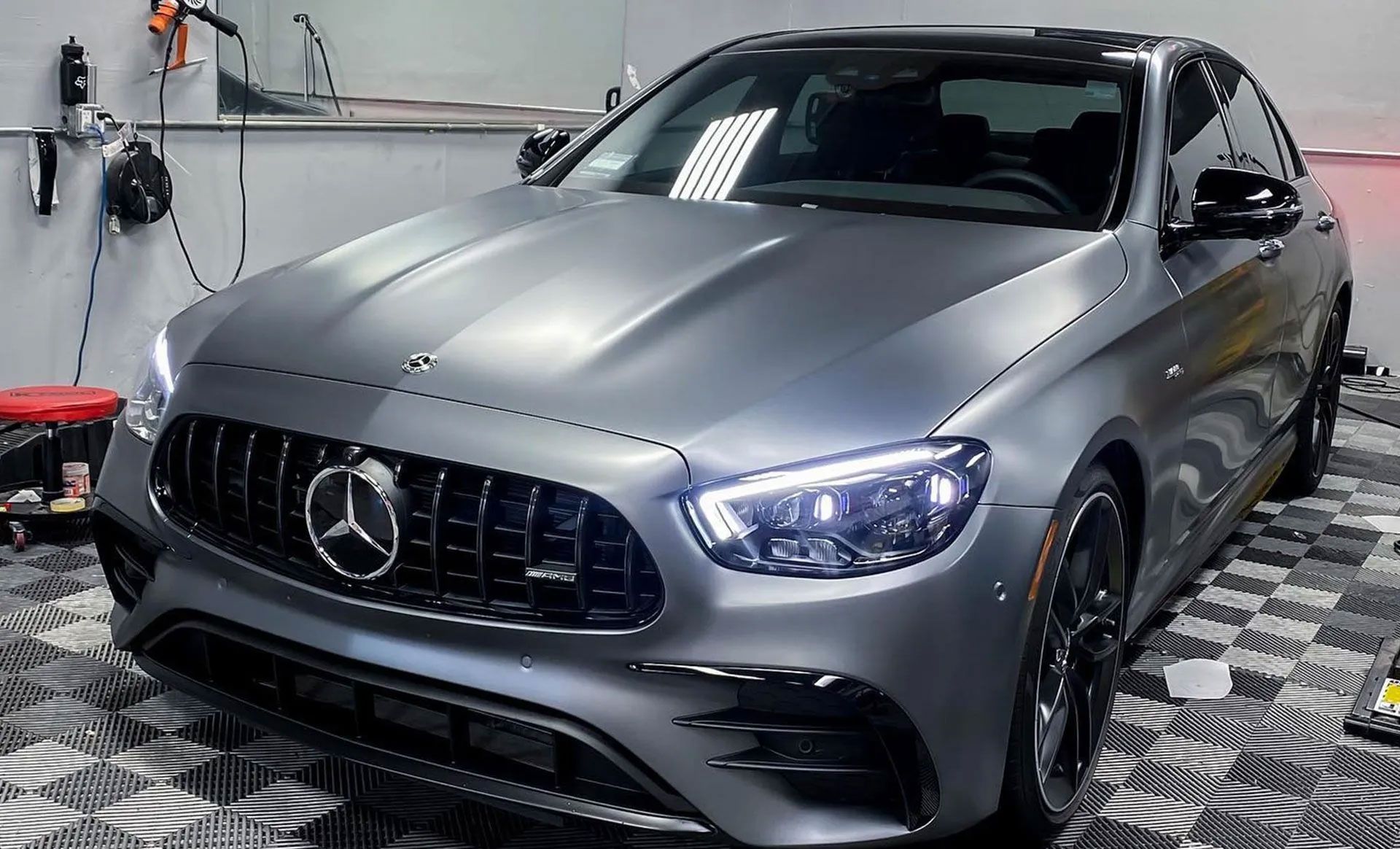 A matte gray Mercedes-Benz E-Class sedan parked in a garage with a checkerboard floor.