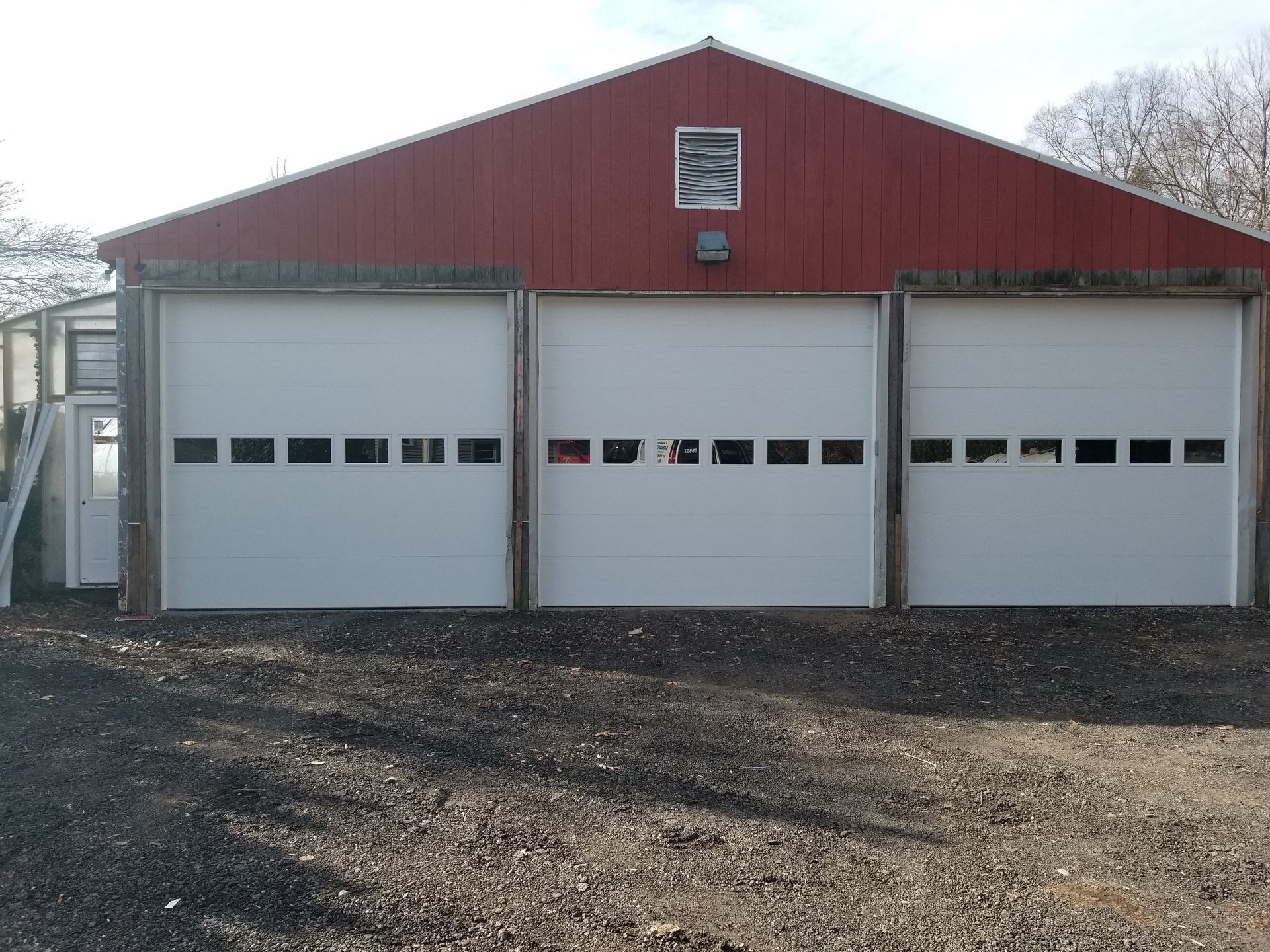 Red barn-style garage with three white overhead doors and a gravel driveway.