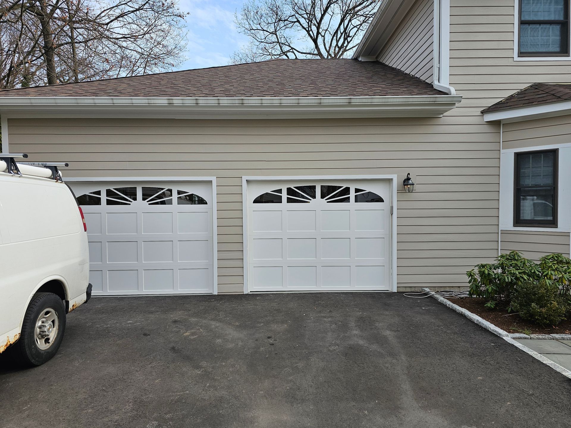 Two-car garage with white doors beside a beige house, with a white van parked on the left.