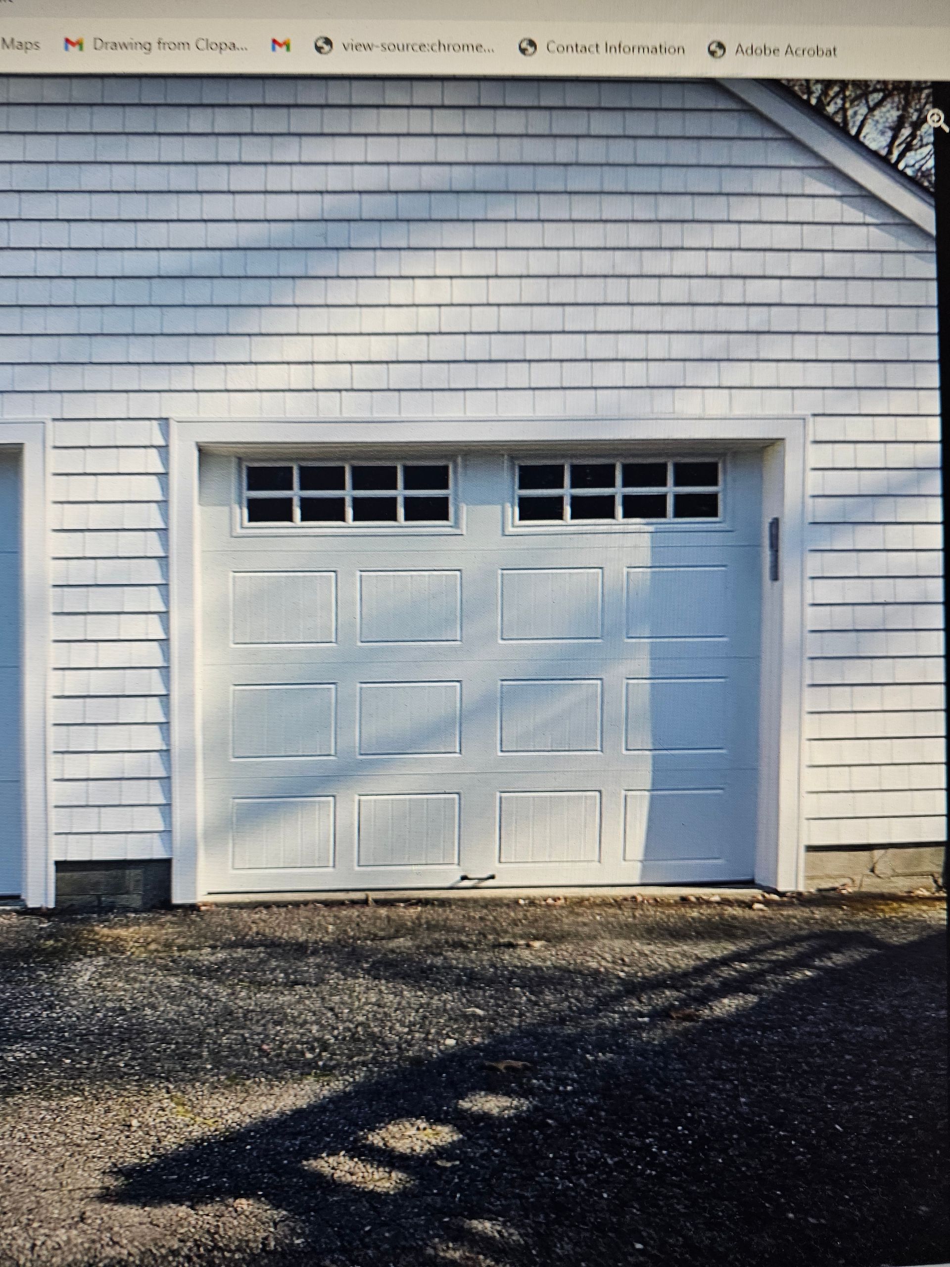 White garage door on a shingled house, with sunlight and shadows on the driveway.
