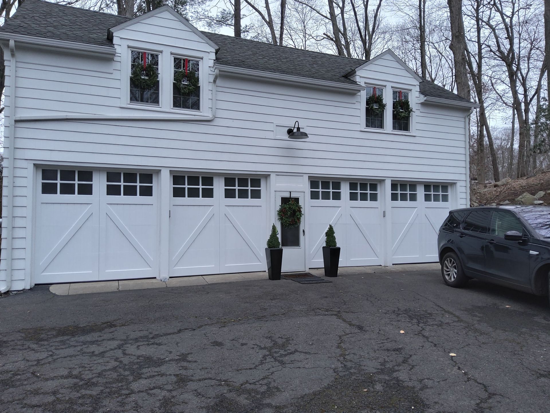 White two-story garage building with dormer windows and a parked SUV on a driveway