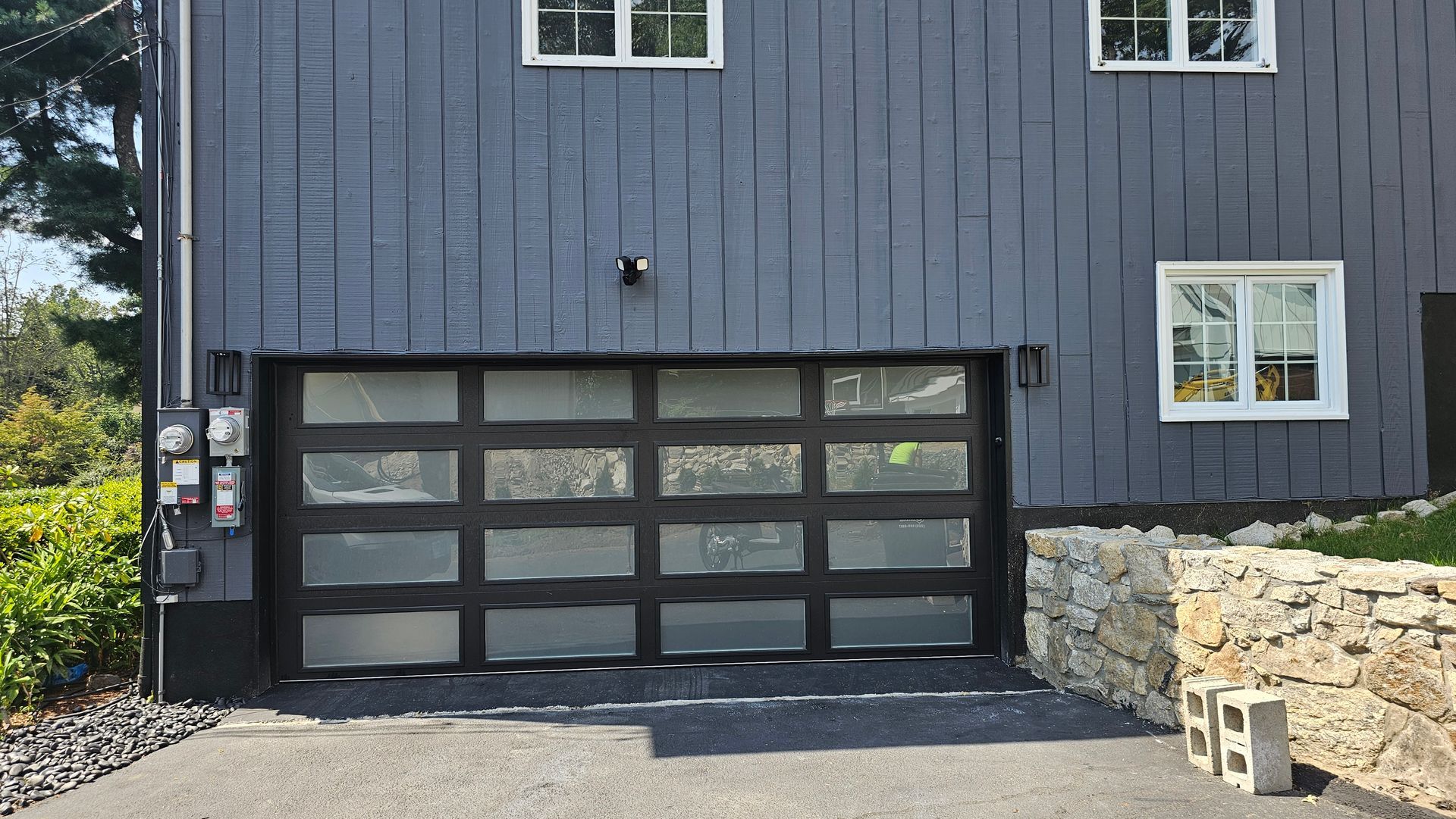 Gray garage door on a dark blue house with stone retaining wall and driveway