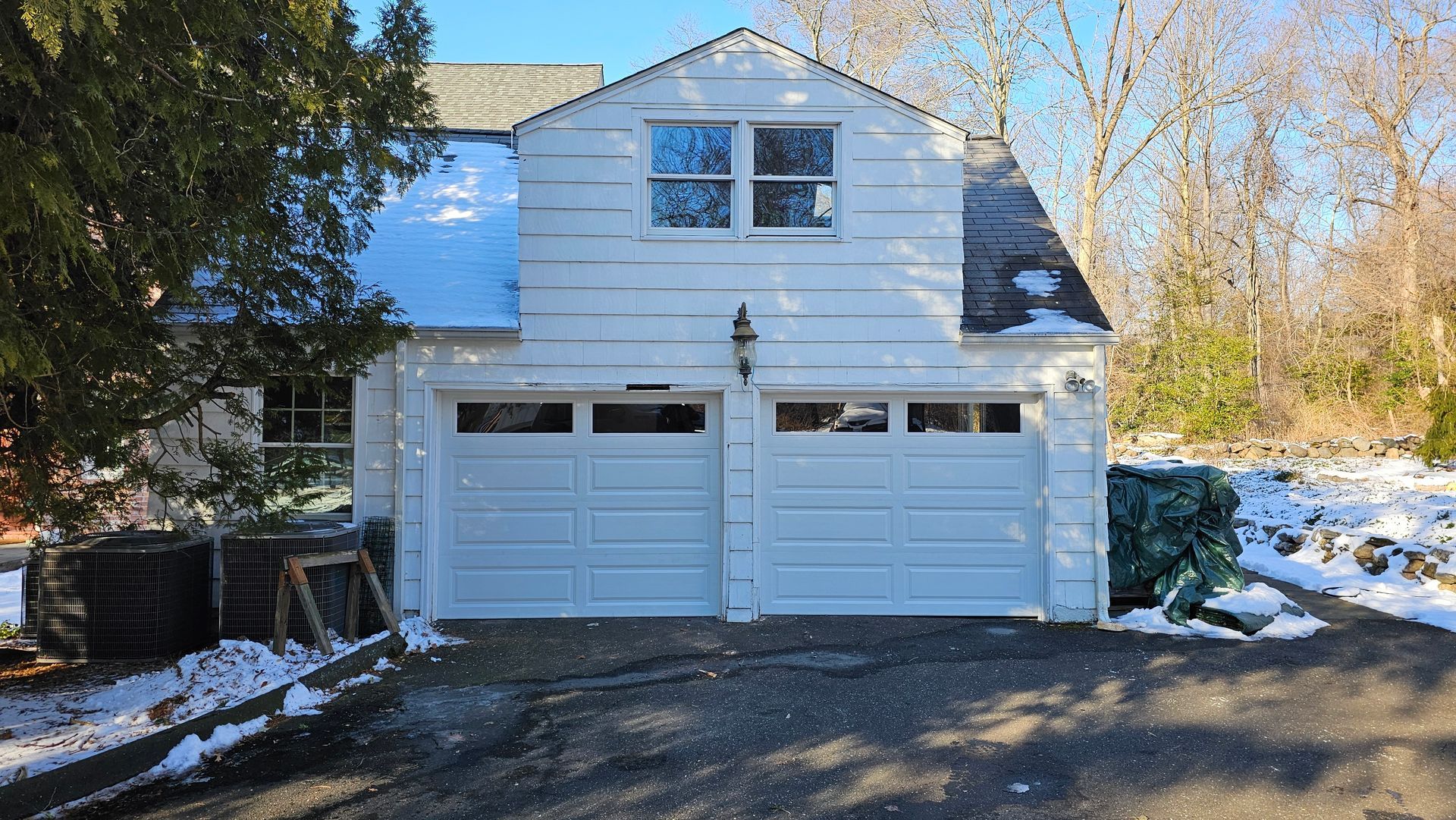 Snow-covered two-story white house with a double garage and trees in the background