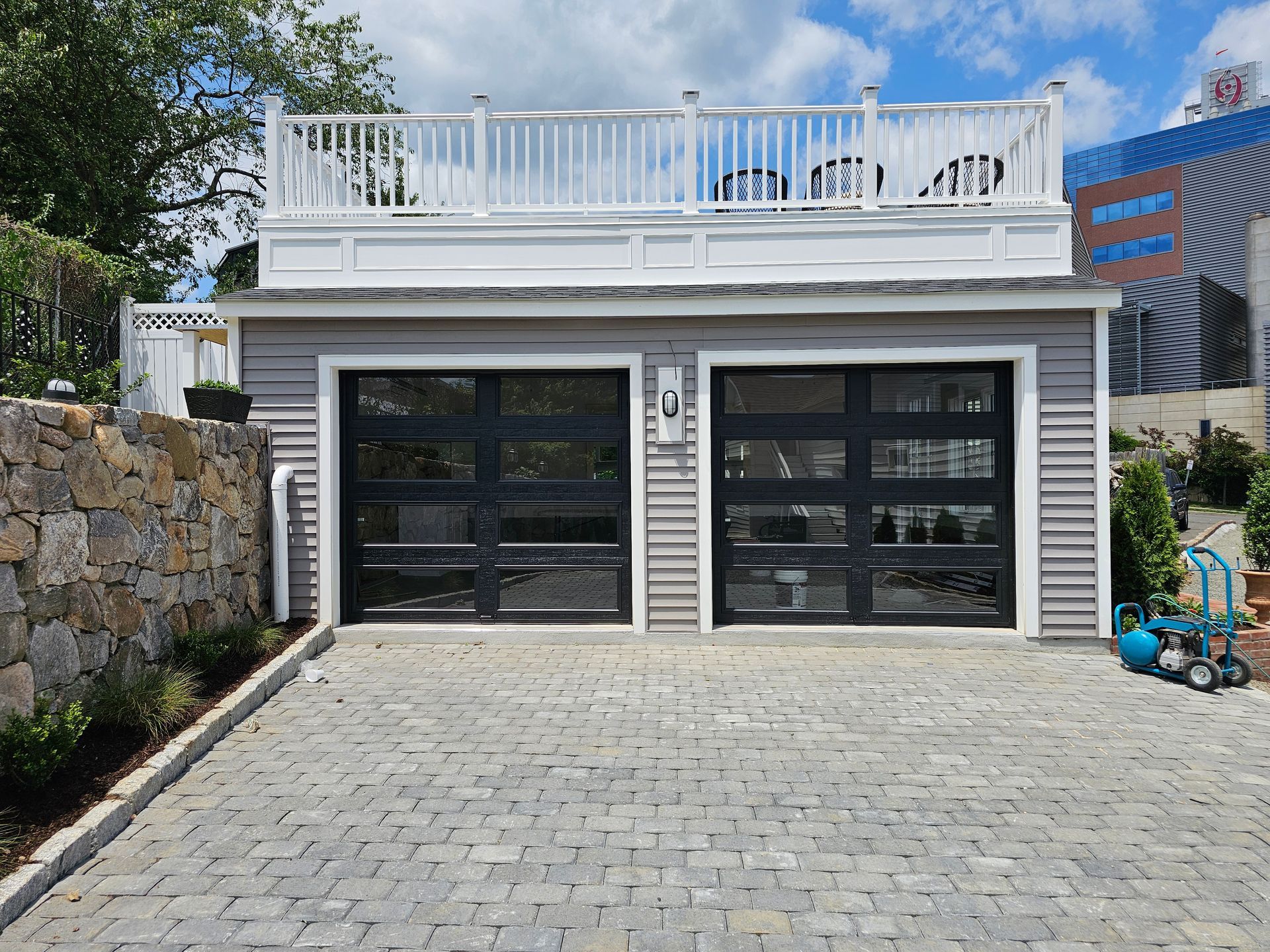 Two-car garage with white deck above, black doors, and paved driveway under a blue sky