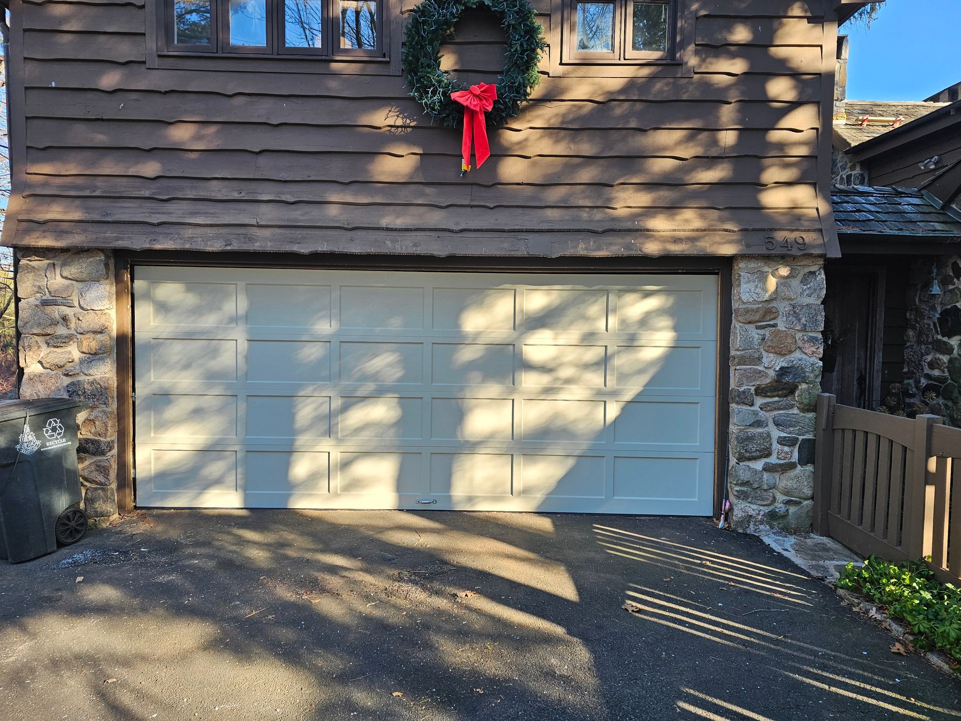 Two-car garage with white doors, stone exterior, and a holiday wreath above the entrance.