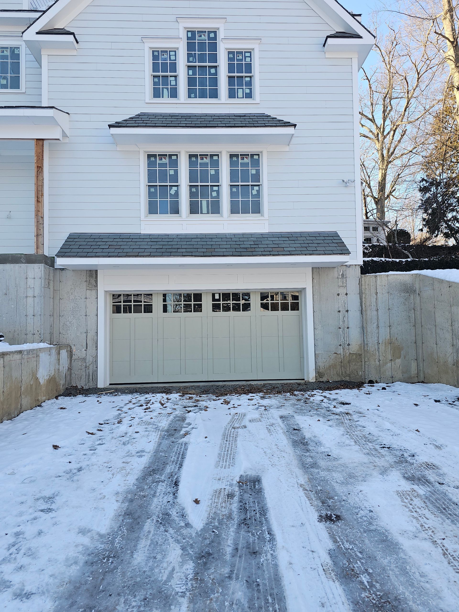 Snow-covered driveway leading to a white garage beside a house with a frost-coated wall