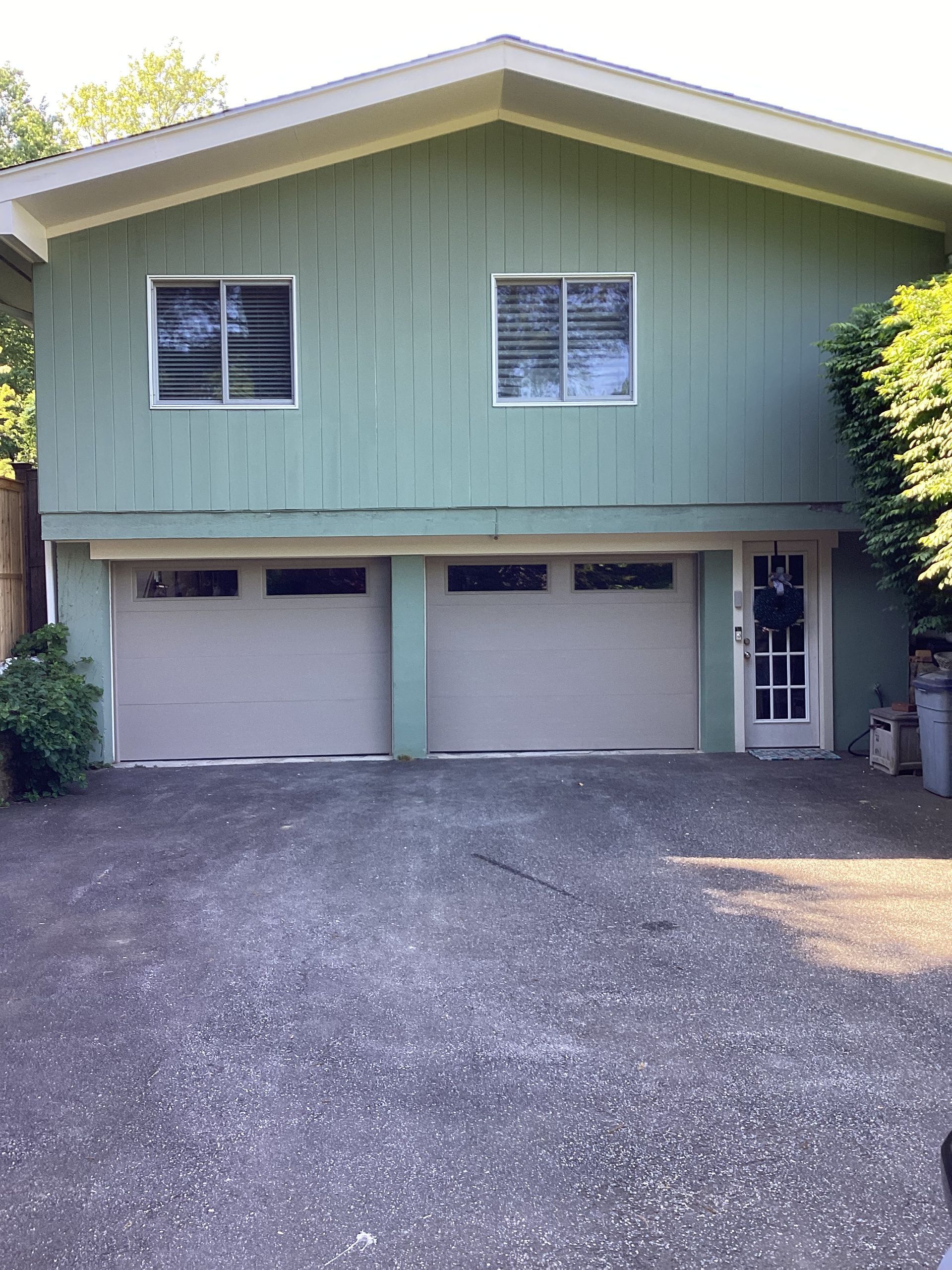Green two-car garage with white trim and a side entry door, viewed from a gravel driveway.