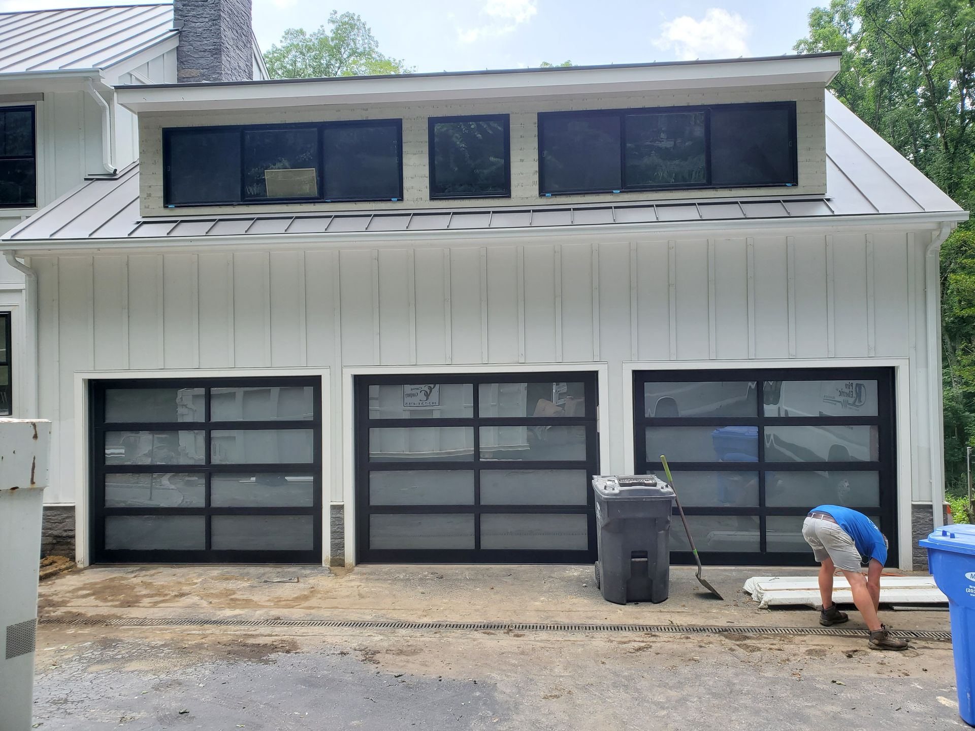 Modern house exterior with three glass-panel garage doors and a person working near the driveway