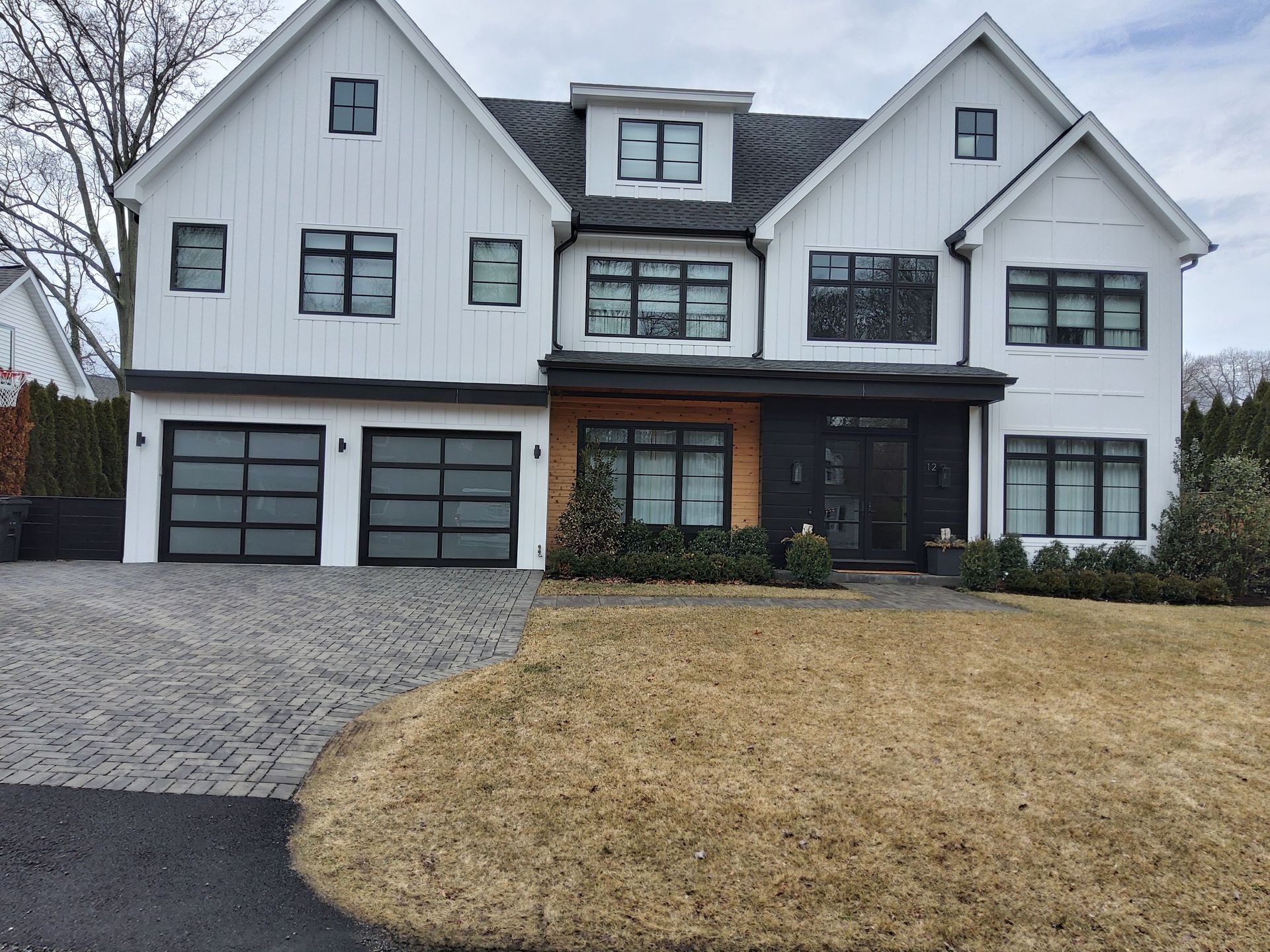 Large white two-story house with dark trim, stone driveway, and brown winter lawn