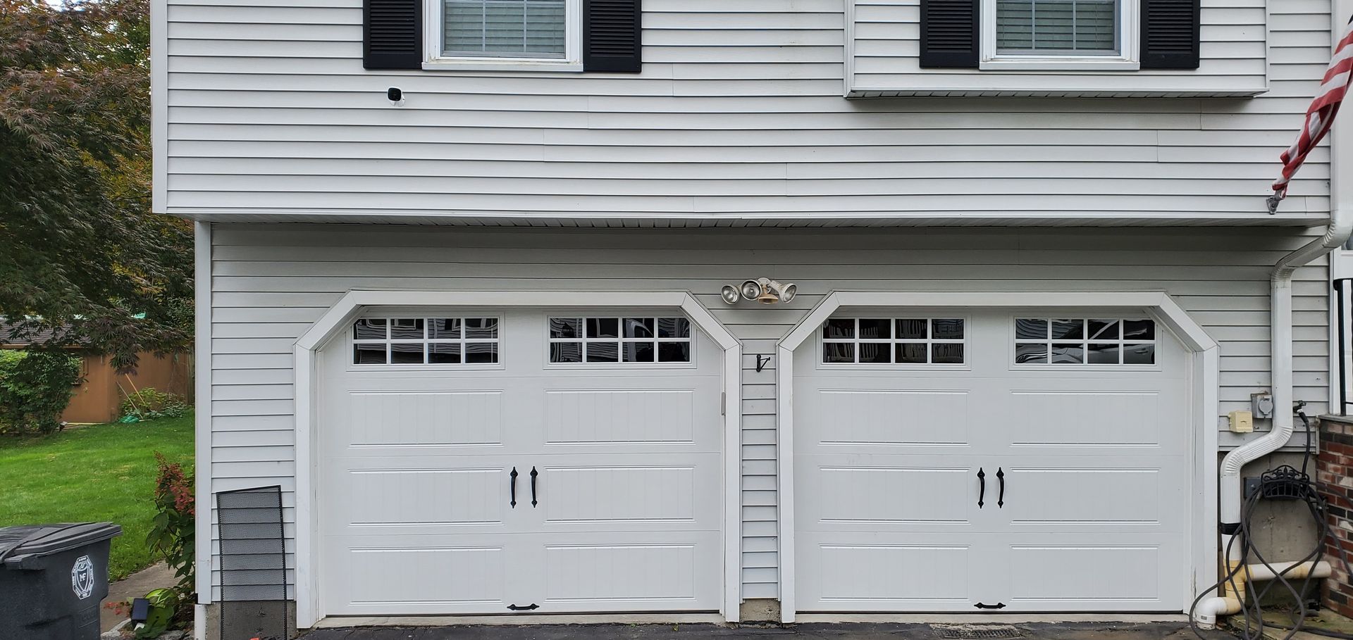 White double garage doors beneath a white house exterior with black shutters and a driveway in front