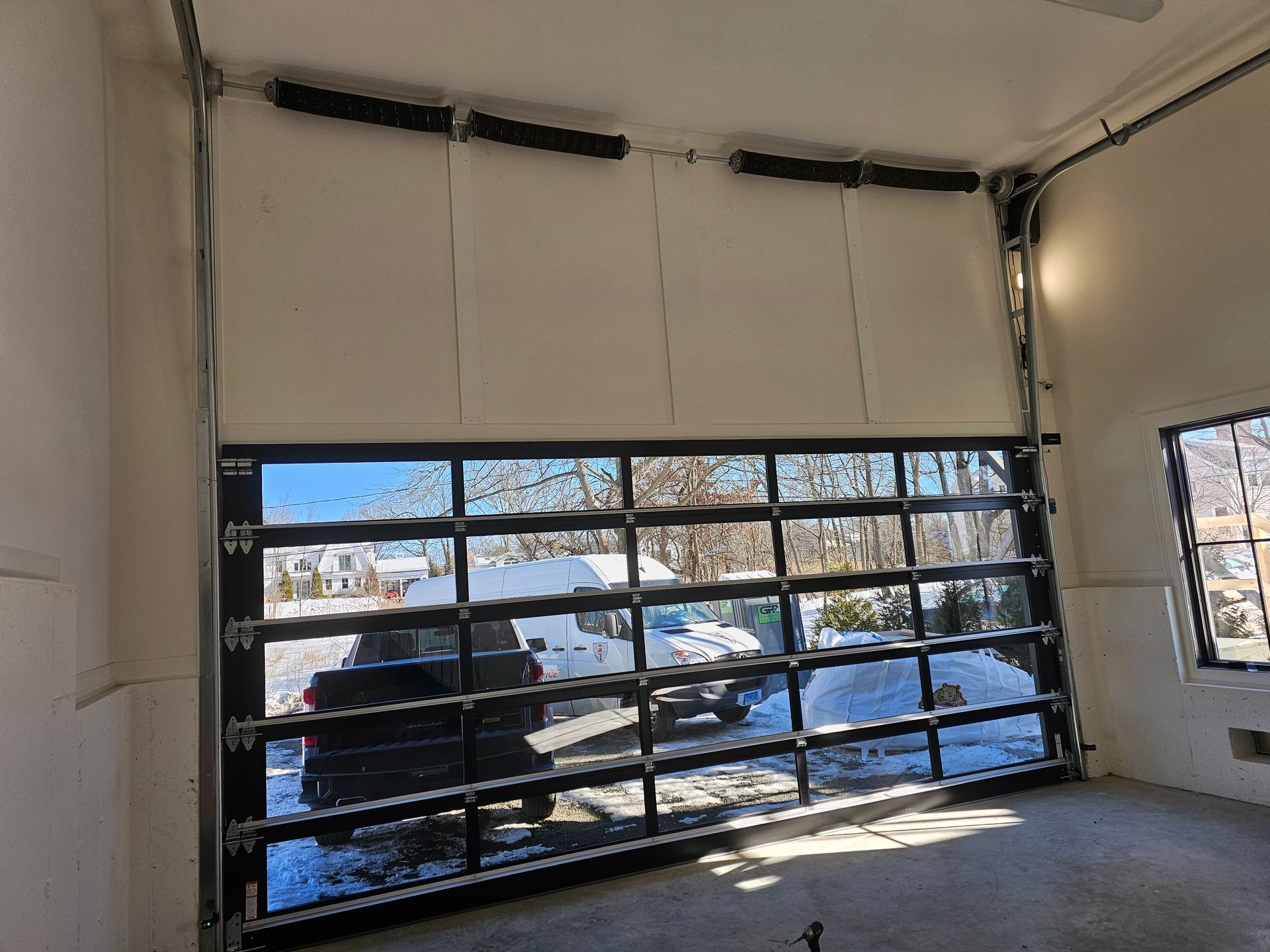 Garage interior with a large glass sectional door and snow visible outside.