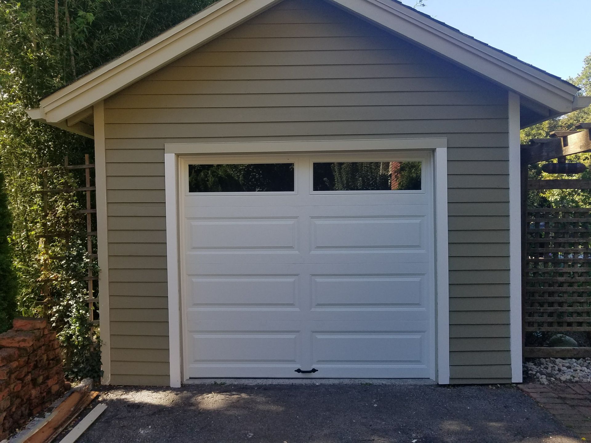 White garage door on a small gray detached garage with a gabled roof and stone driveway.