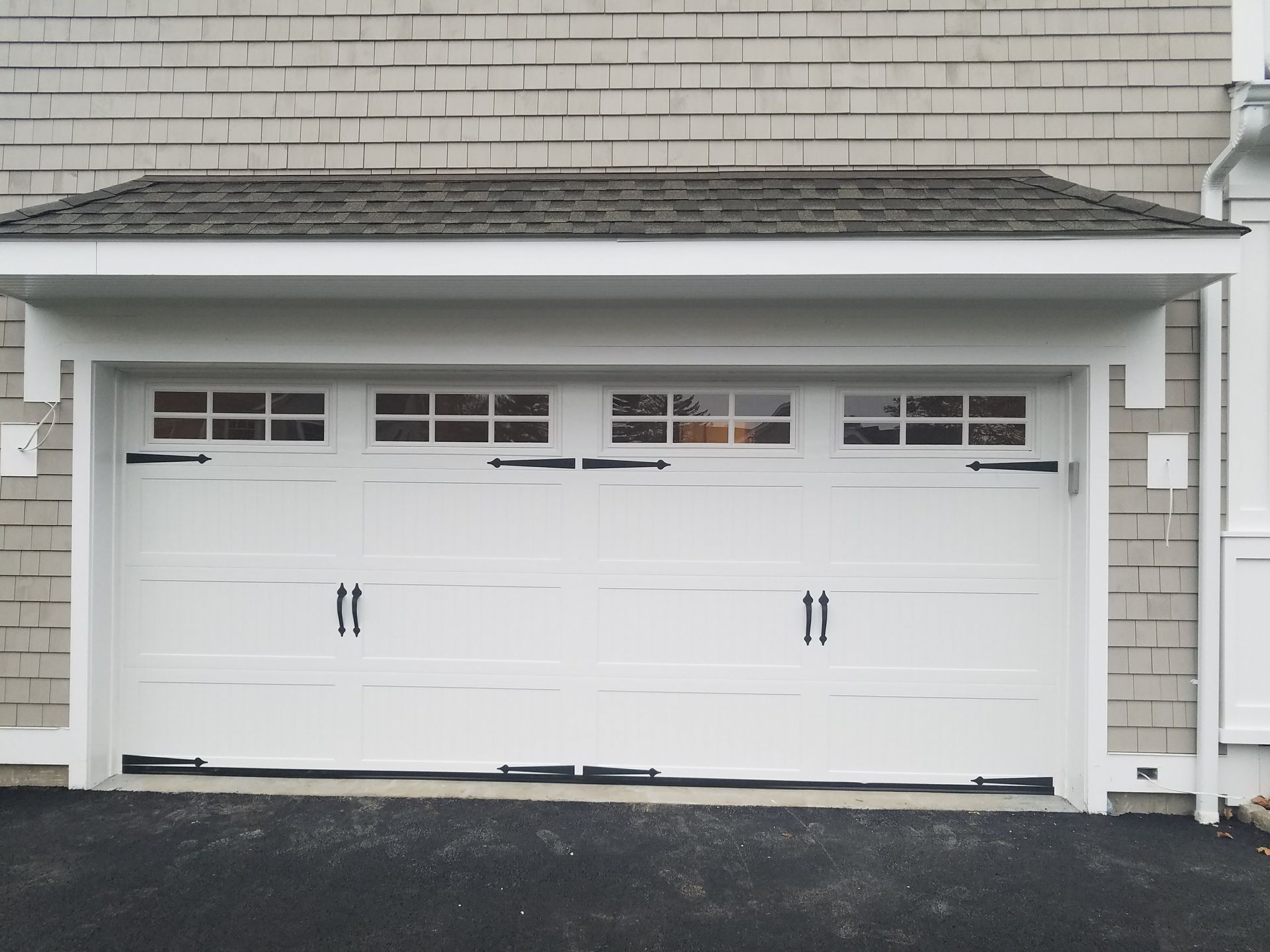 White three-car garage door on a light gray house exterior with small windows above the panels.