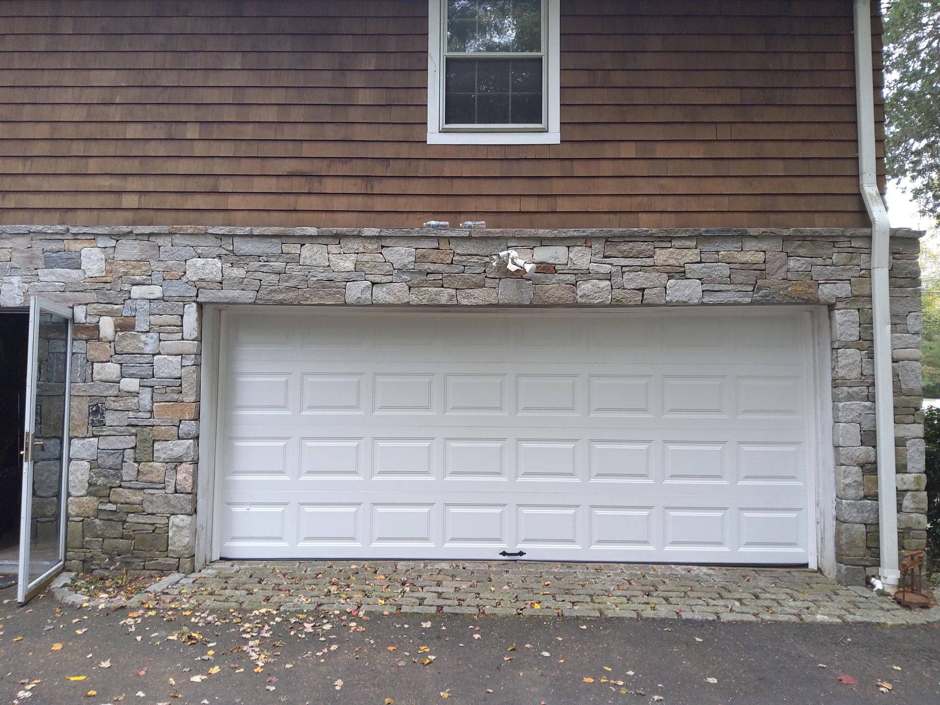 Stone-front house with white two-car garage door and brown shingled siding