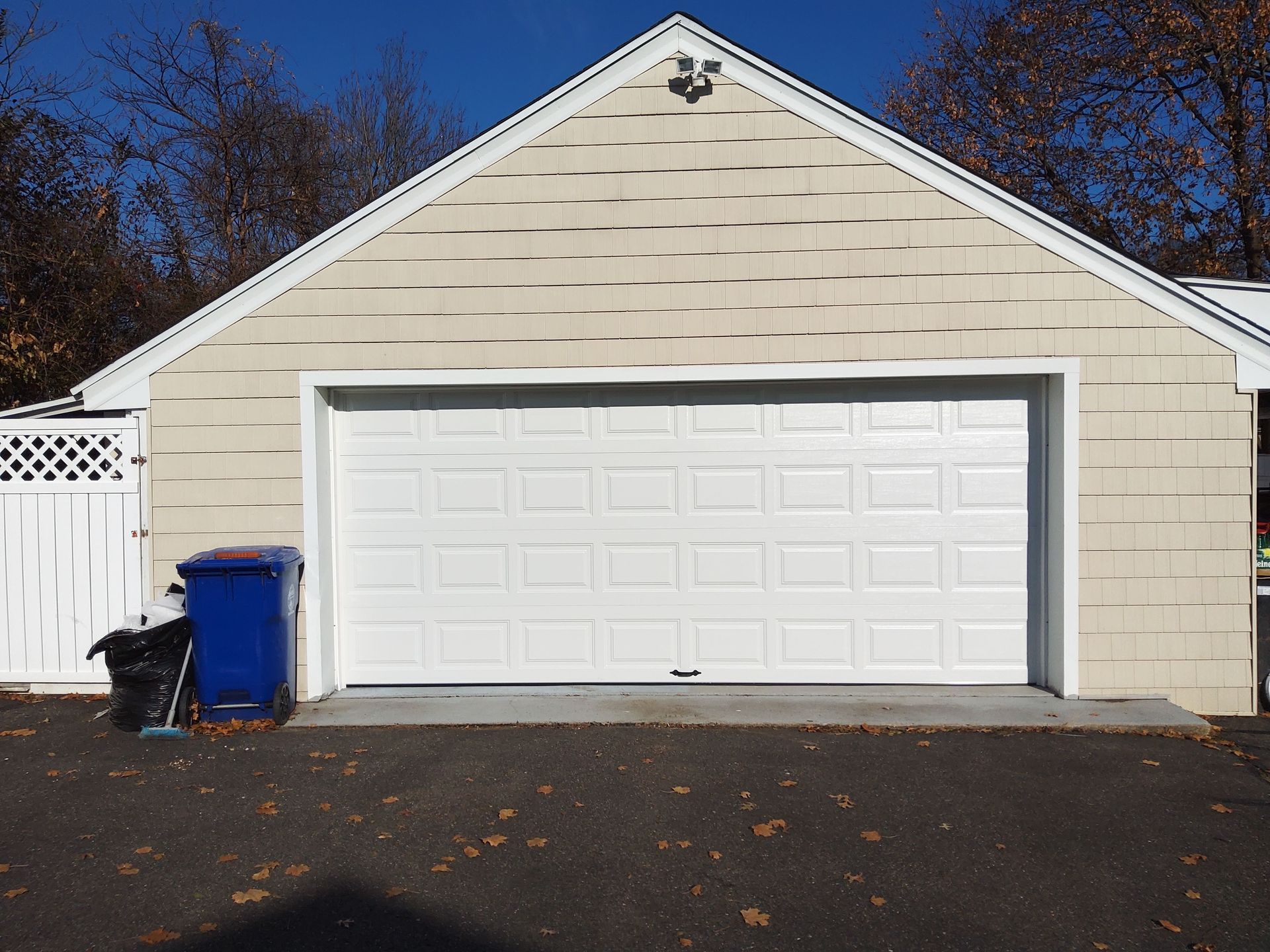 White garage with a double door and blue trash bin on a driveway, viewed from the front.