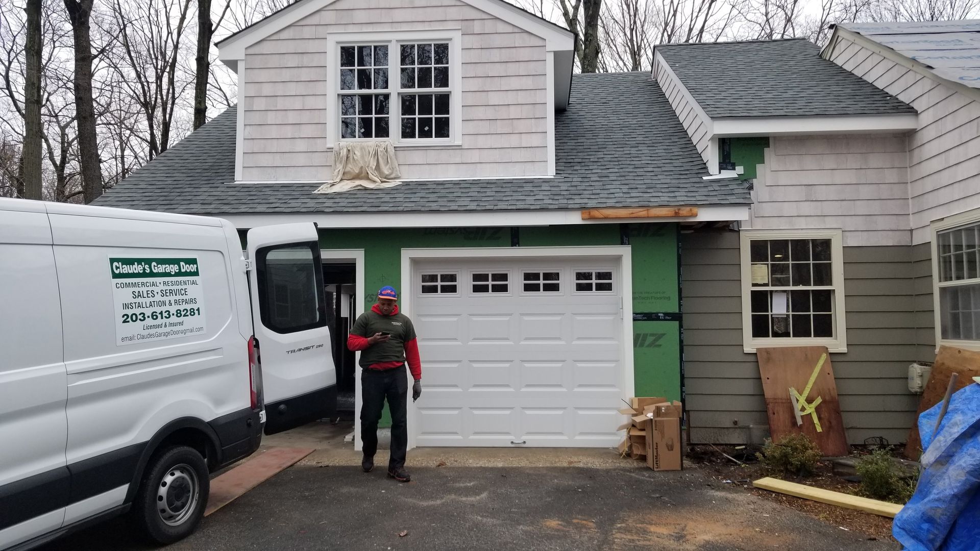 Worker near white service van outside a house with garage, holding a red tool bag