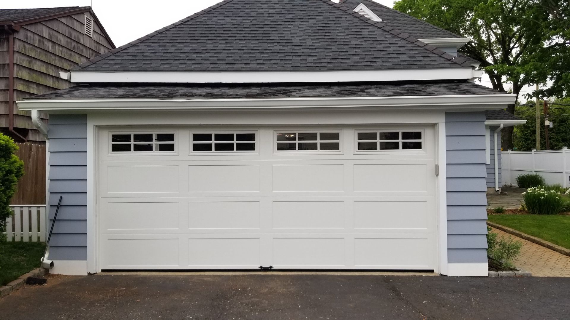 White double garage door on a light blue house with a gray shingled roof and driveway.
