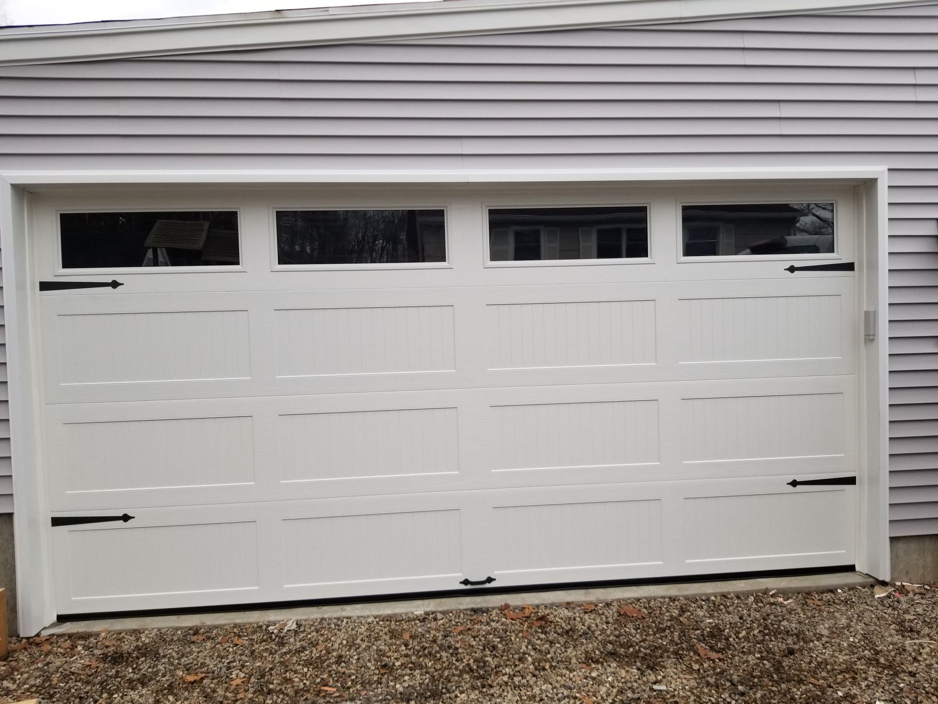 White double garage door with four small windows at the top, on a house exterior.