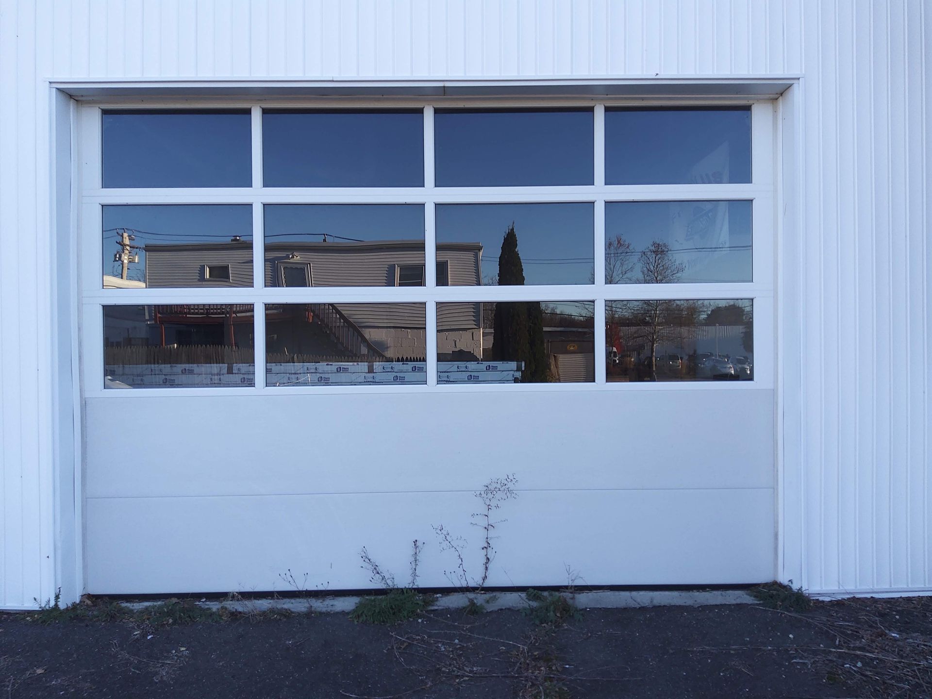 White garage door with four window panes on a metal-sided building, reflecting the street outside