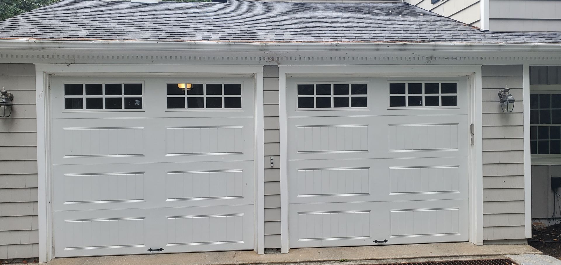 Two white garage doors on a beige house with snow on the roof