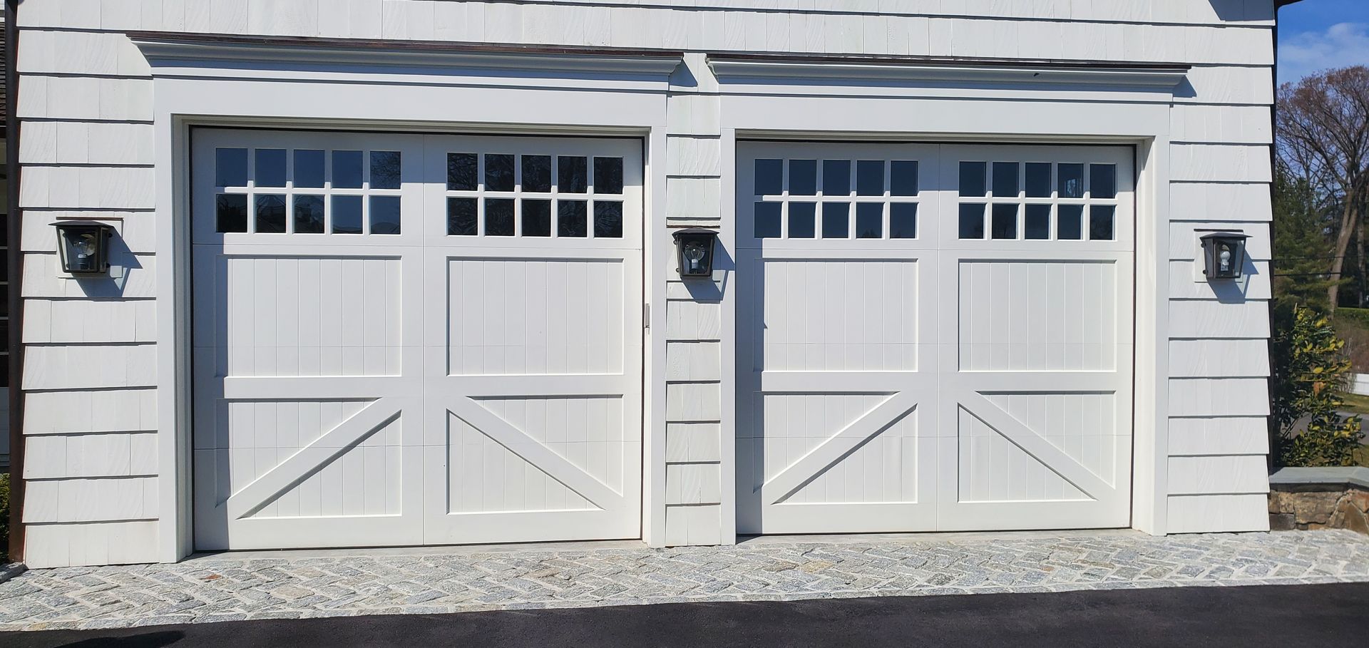 White double garage doors with small windows on a light-sided house exterior.