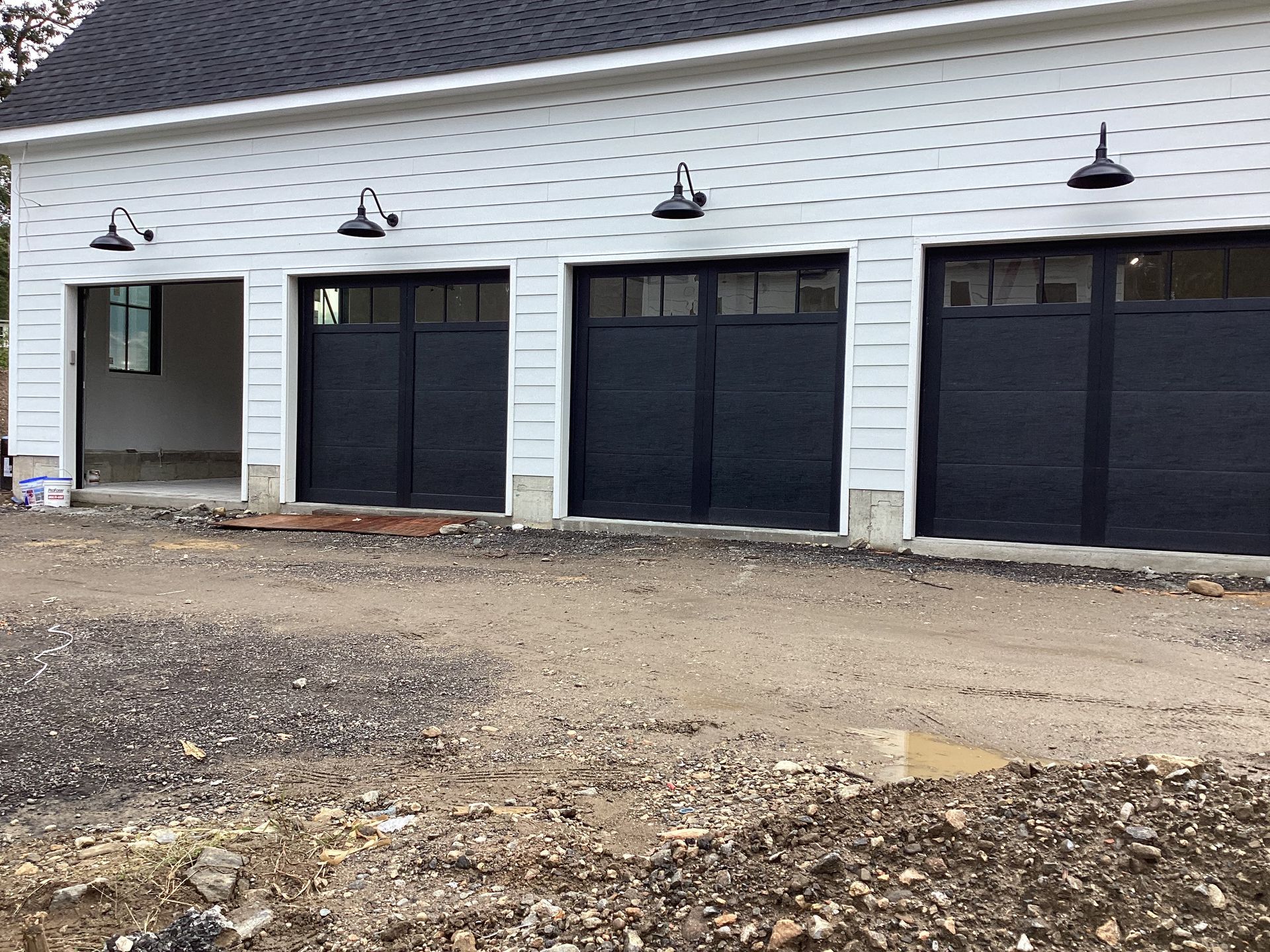 Row of black garage doors on a white building, with gravel ground in front.