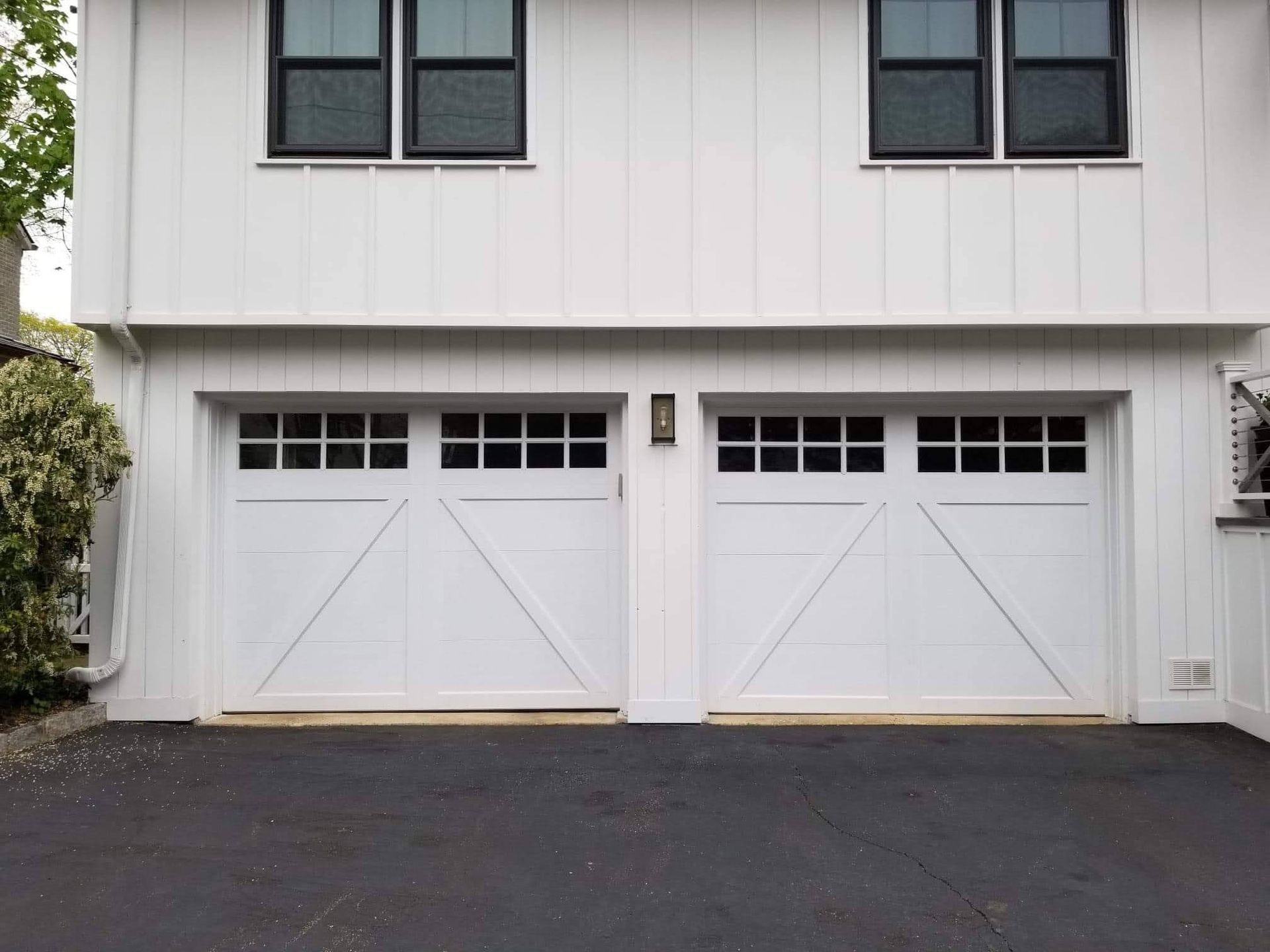 Two white garage doors on a house exterior with white siding and black asphalt driveway