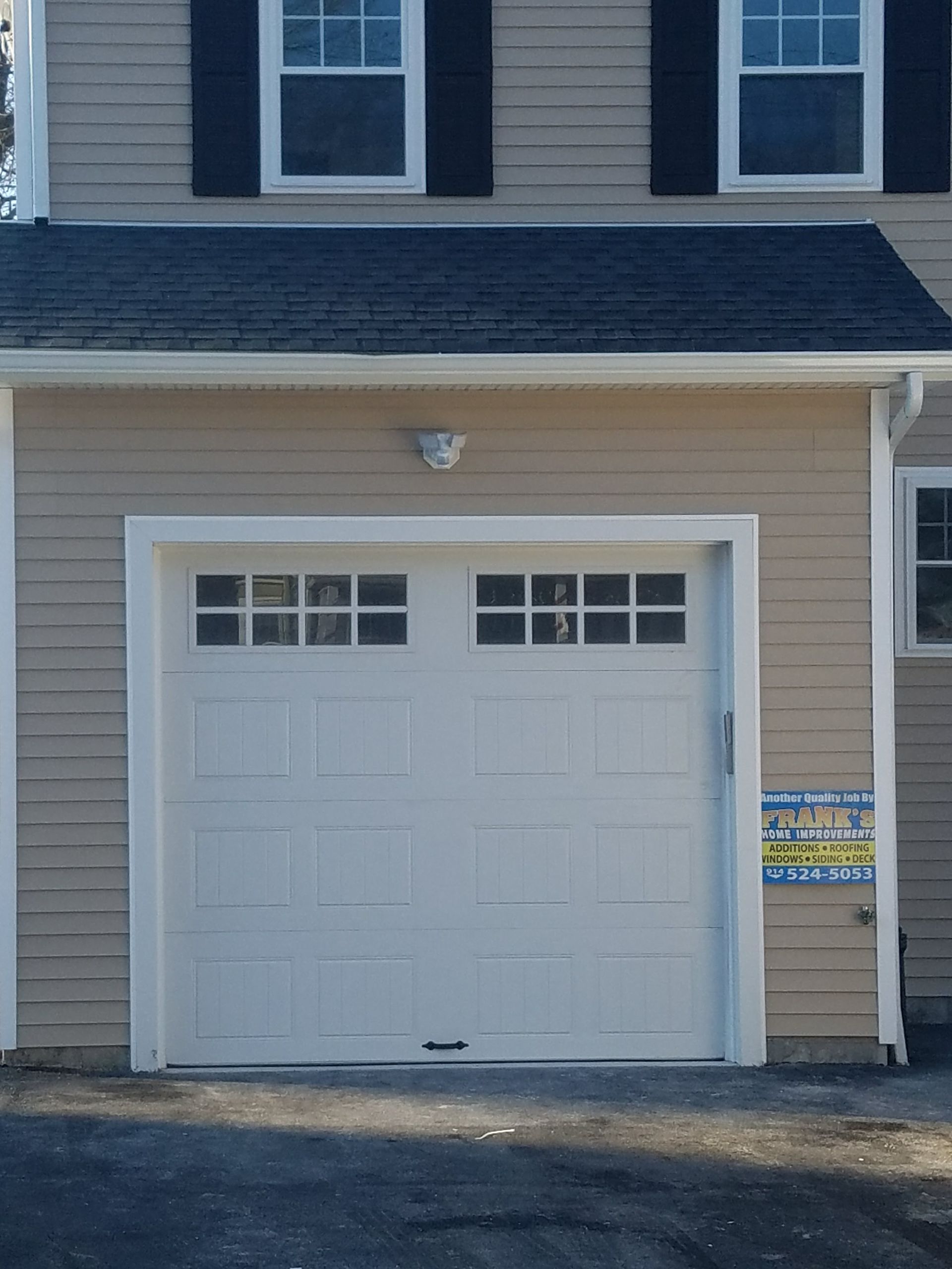 House garage with white door and beige siding under a dark shingled roof